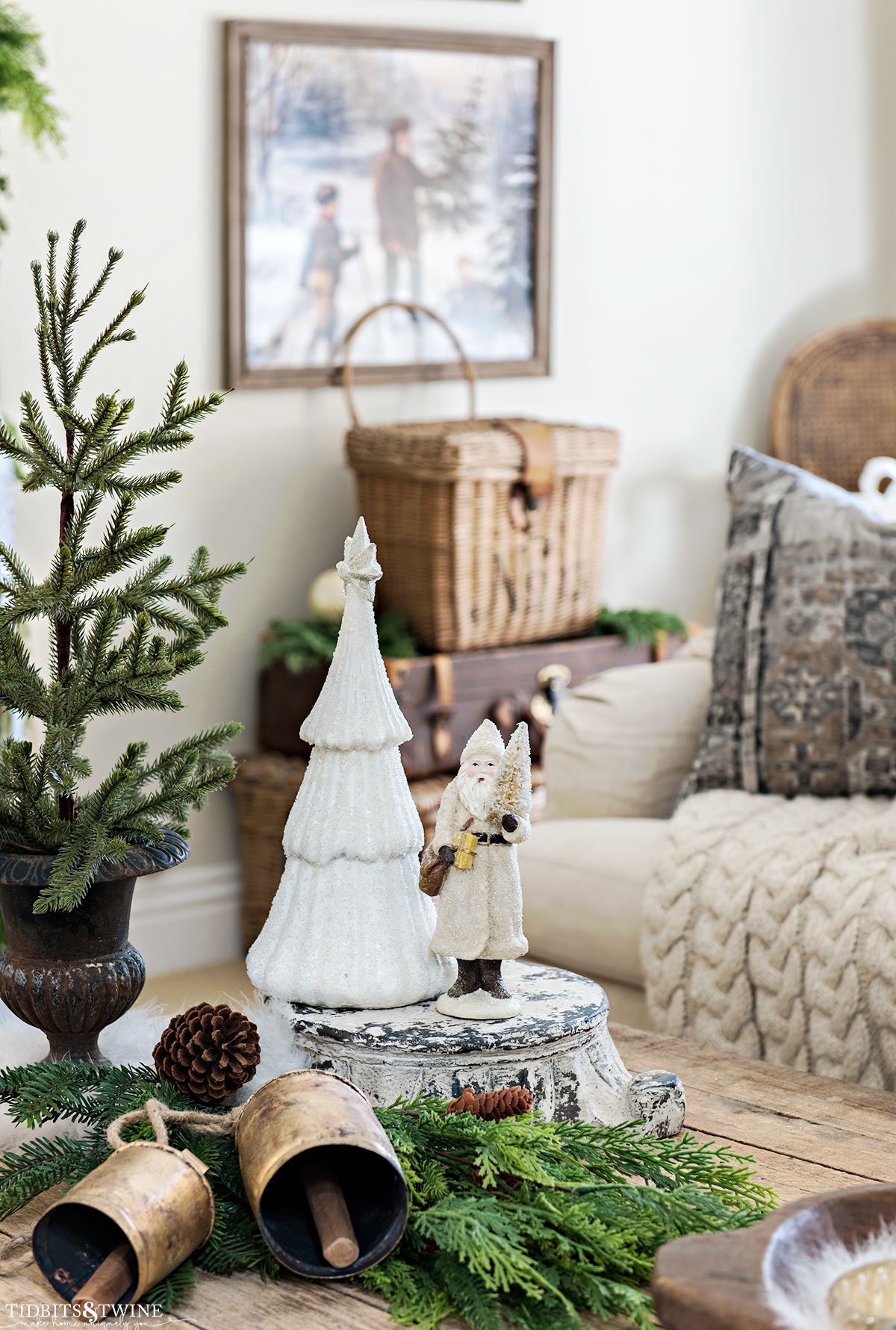 Christmas vignette on coffee table featuring vintage-style Santa, white tree figurine, greenery, and brass bells