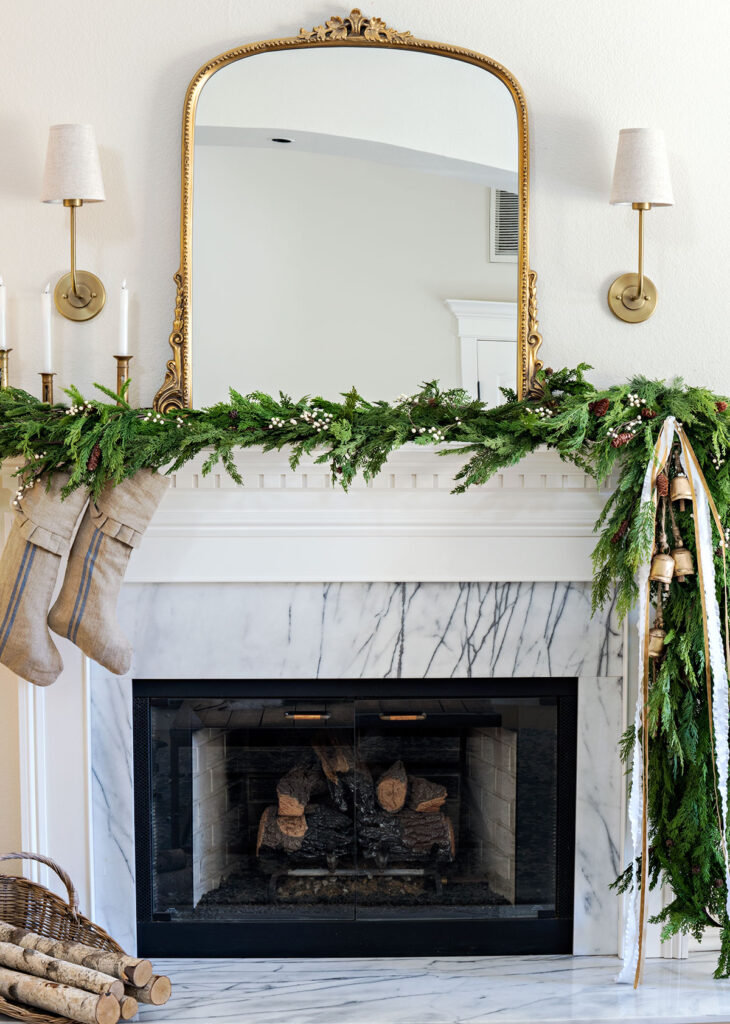 christmas living room fireplace with garland on the mantel and gold anthropologie mirror flanked by sconces