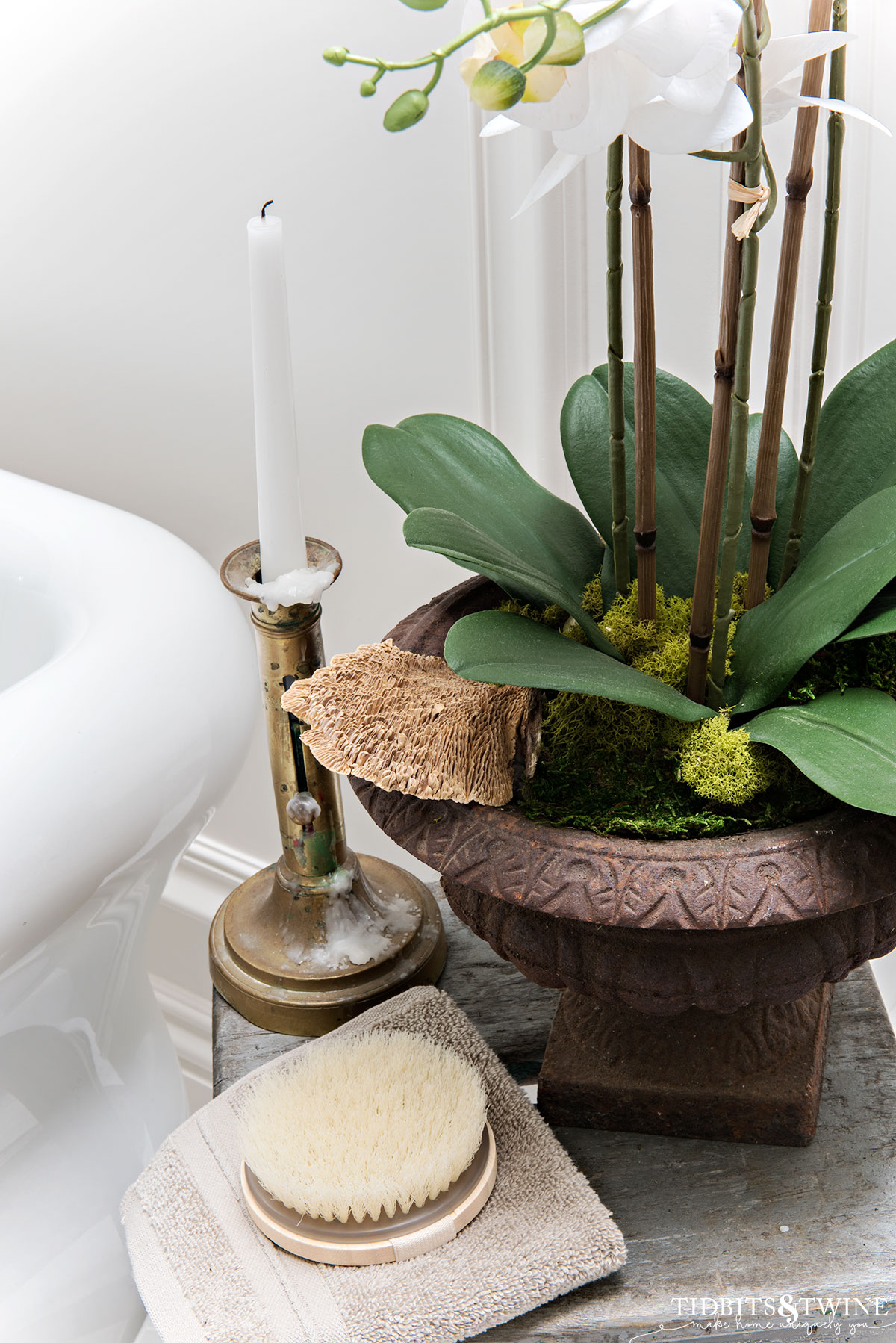 vignette next to bathtub with orchid in a french urn a candlestock and a brush
