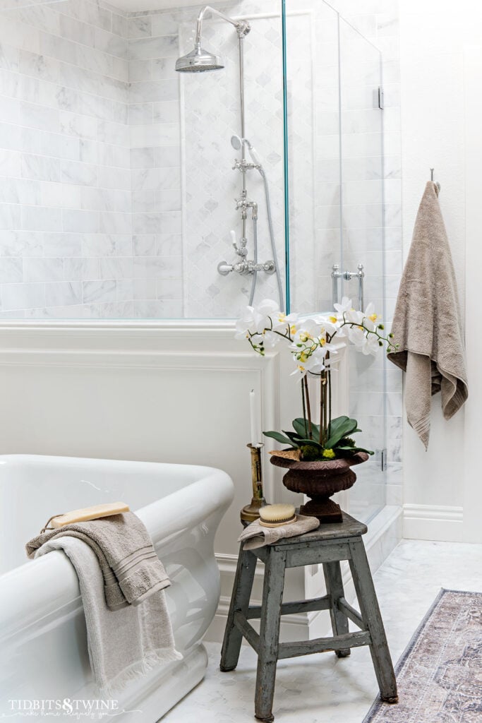 carrara marble shower with pony wall next to freestanding tub with exposed pipe shower