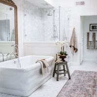 carrara marble primary bathroom with freestanding tub chandelier and large french mirror