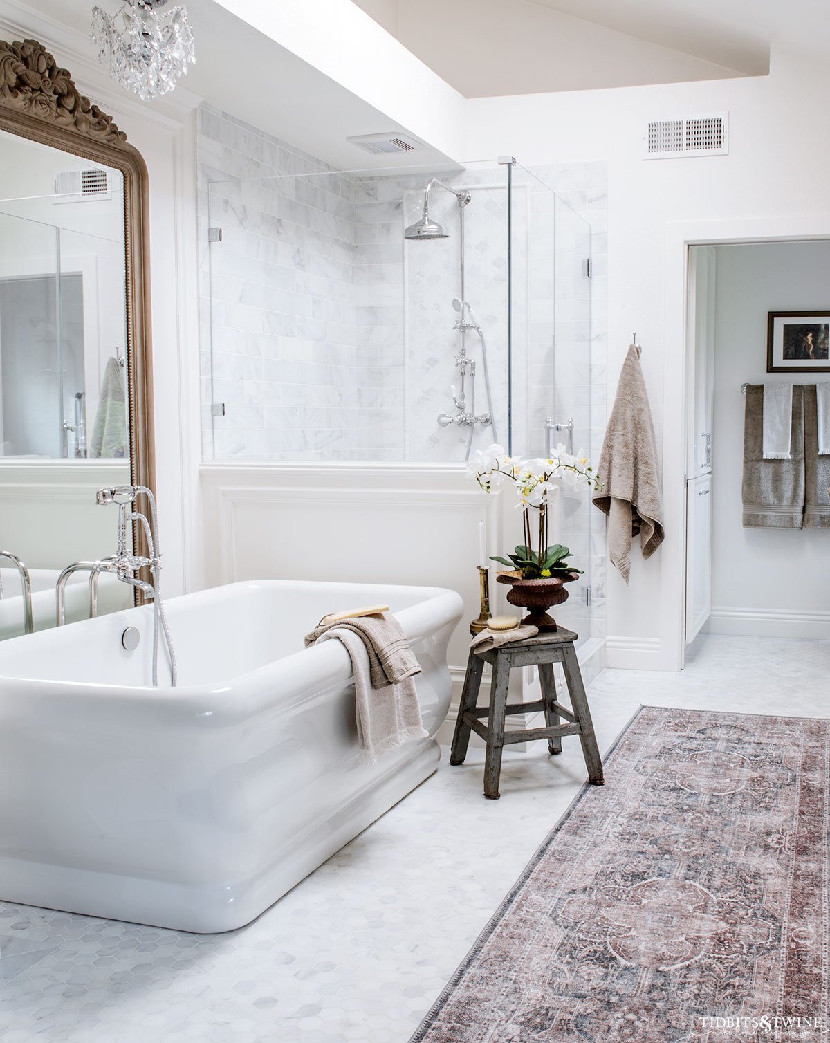 carrara marble primary bathroom with freestanding tub chandelier and large french mirror