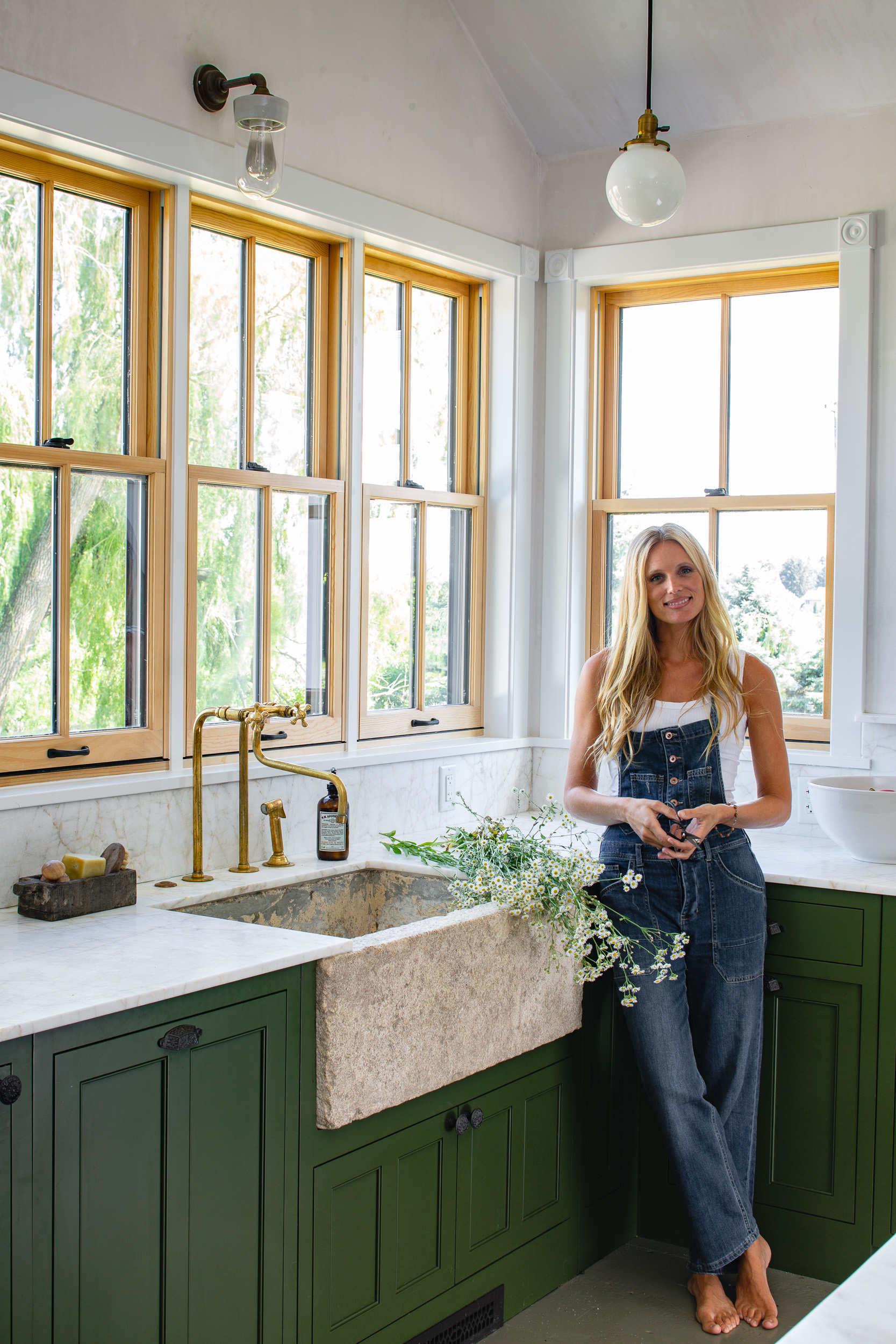 designer lauren liess standing in kitchen with green cabinets and unlacquered brass faucet