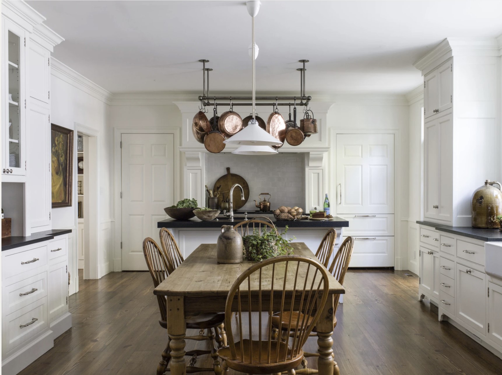 white kitchen with antique wood table and copper pots with wood floors and black countertops