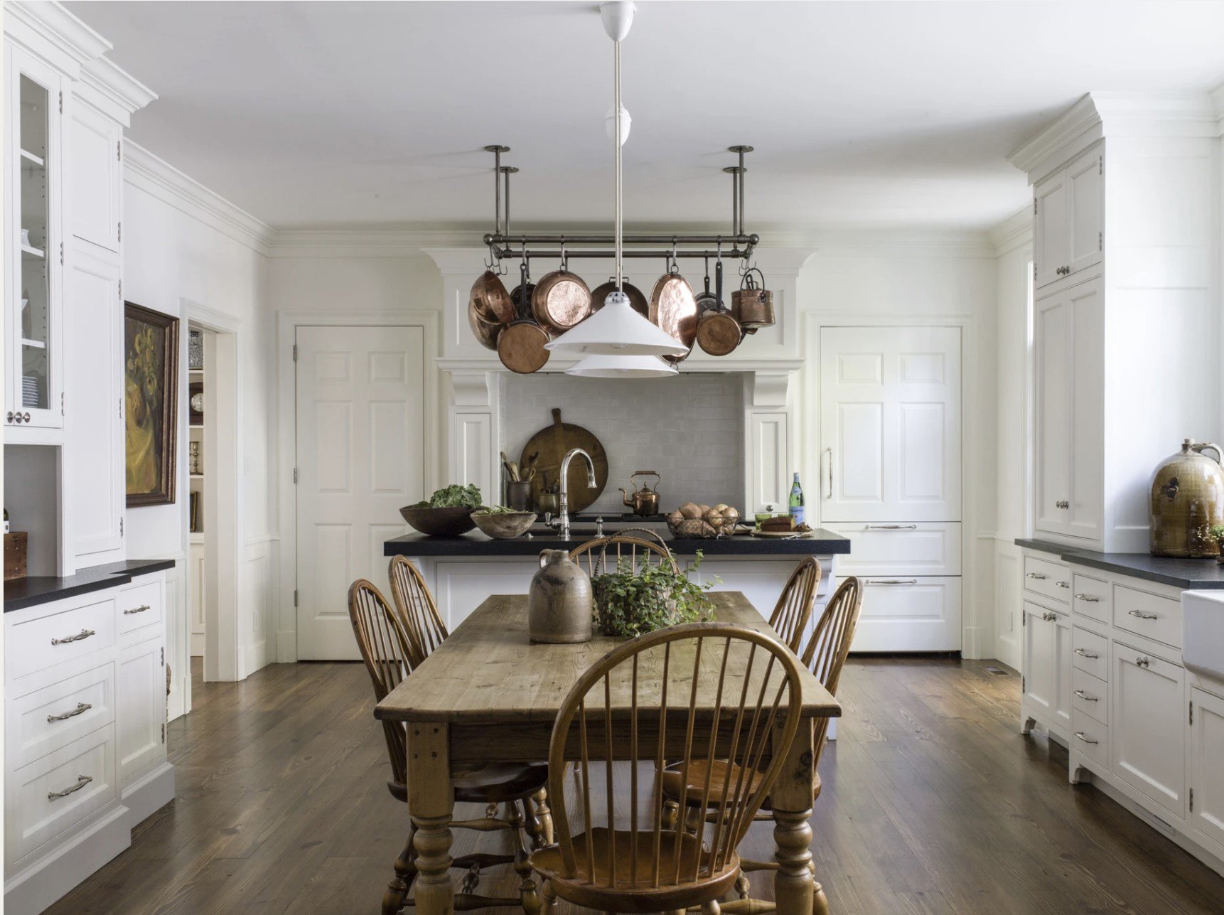 white kitchen with antique wood table and copper pots with wood floors and black countertops