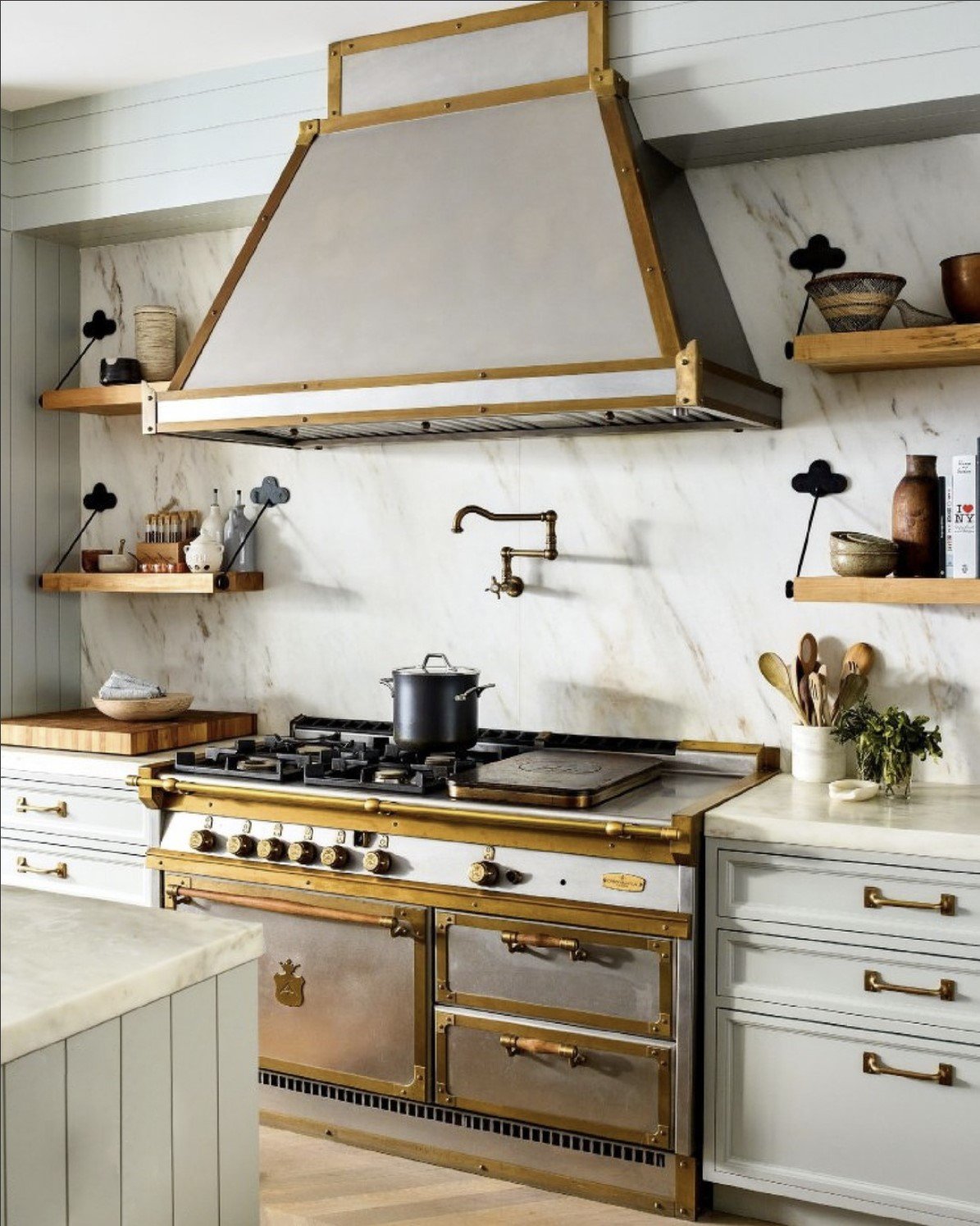 large italian range and hood in kitchen with marble backsplash and floating shelves