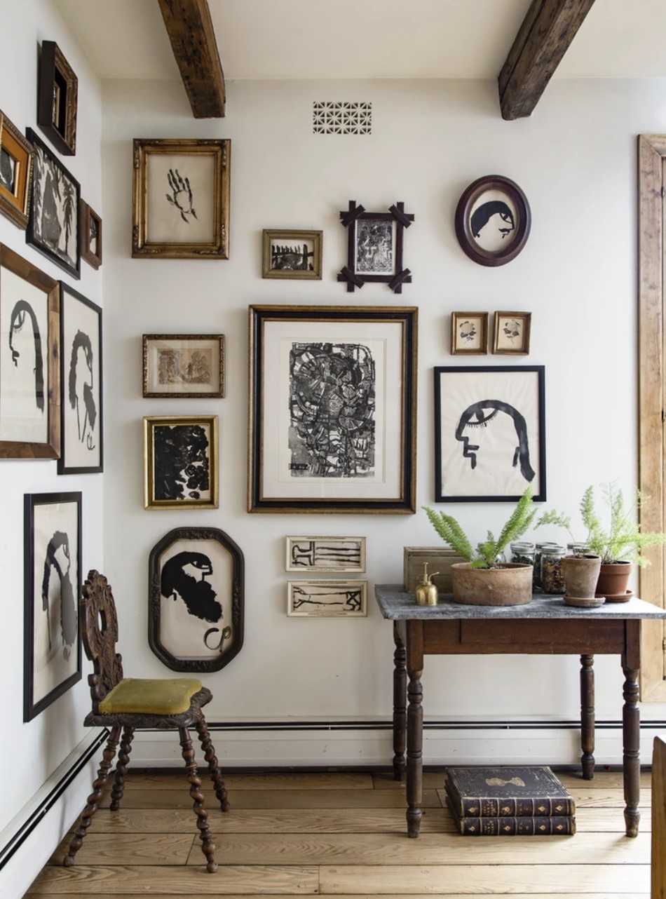 Corner of room with white walls and black white and gold gallery wall with antique table and chair