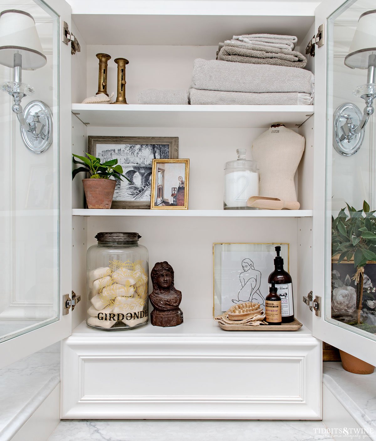 white bathroom cabinet styled with art towels soaps and french vintage items