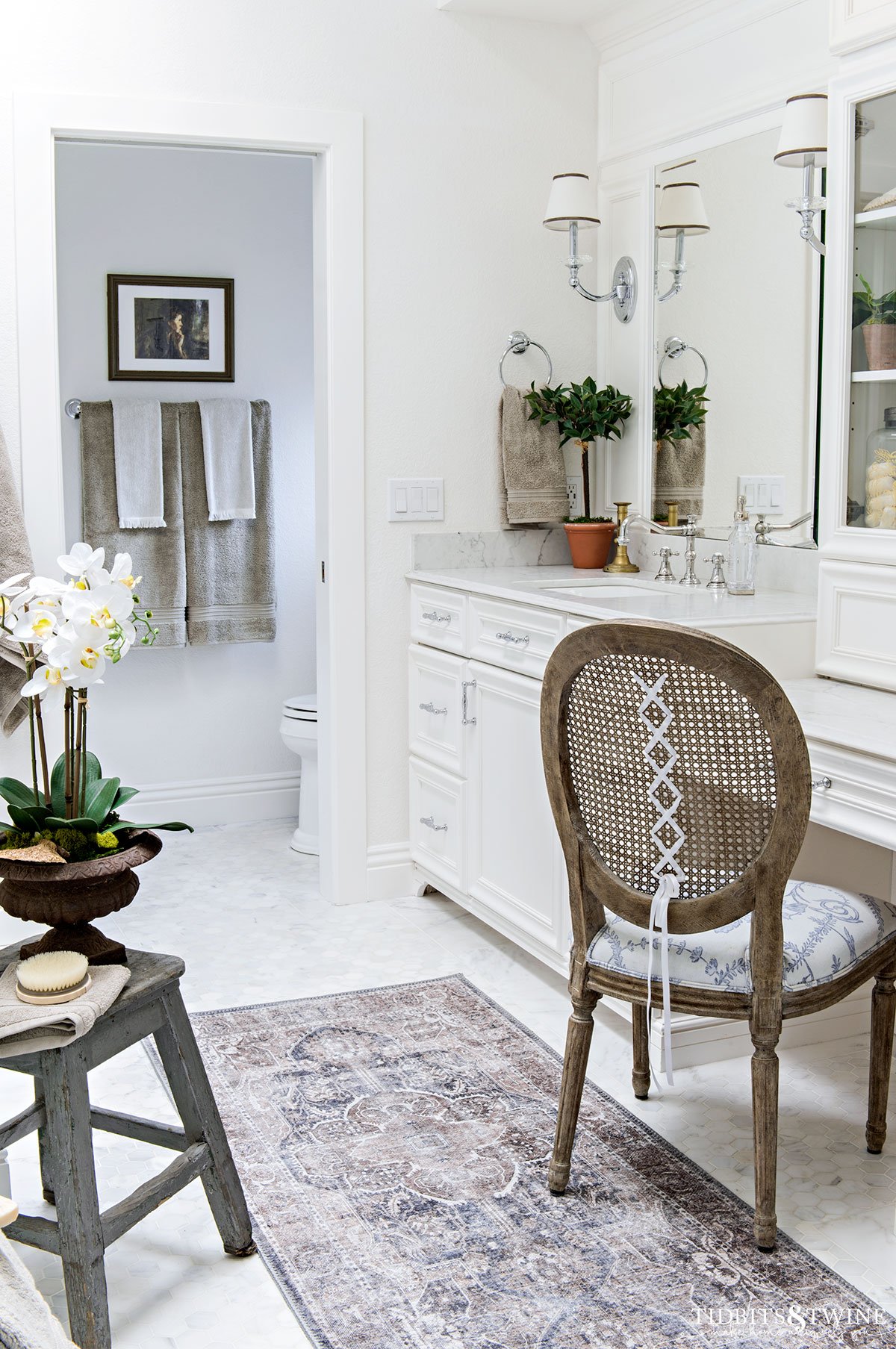 white marble bathroom floor with white vanity and cane back french chair
