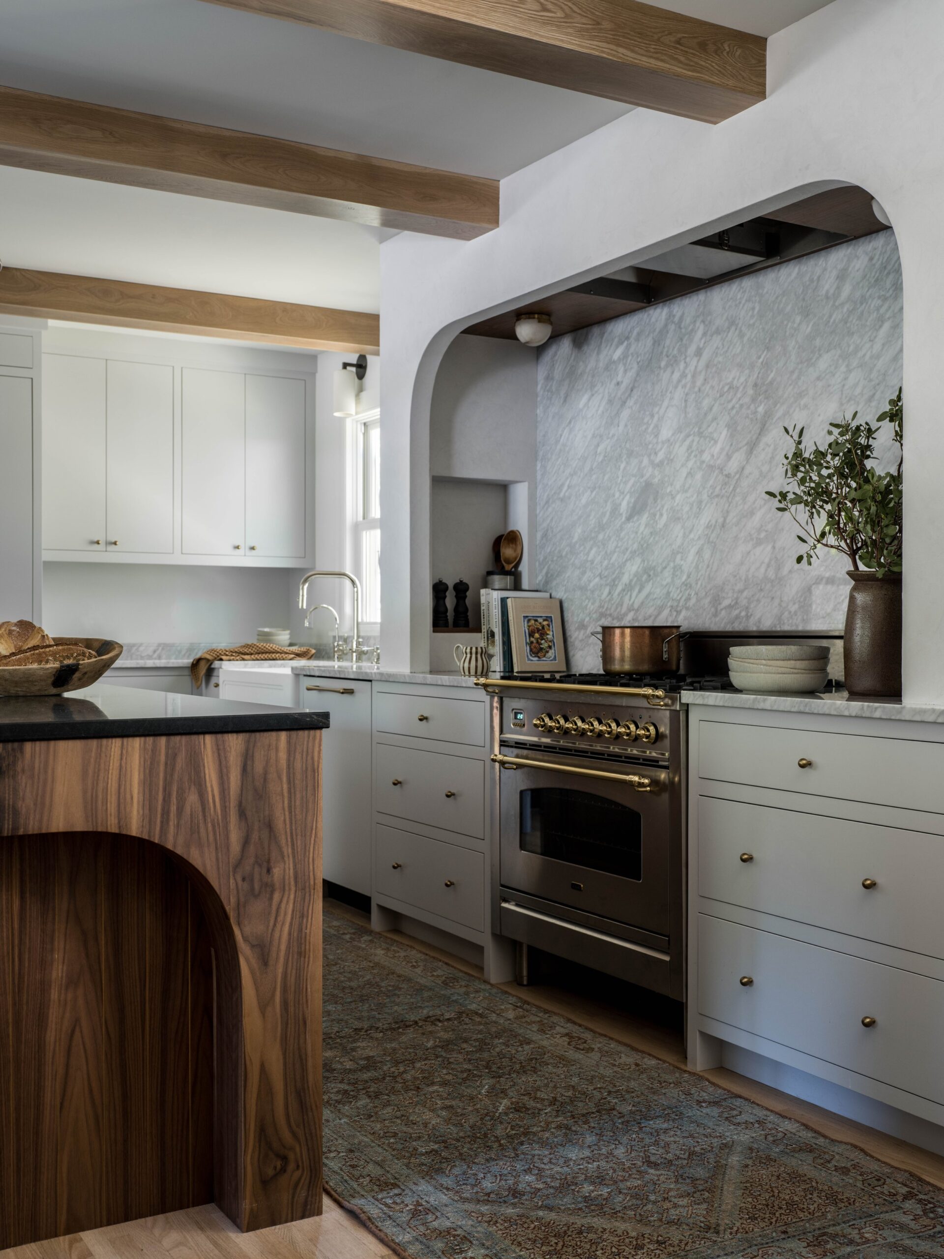 kitchen with white cabinets and stained island and wood beams with arch over stove