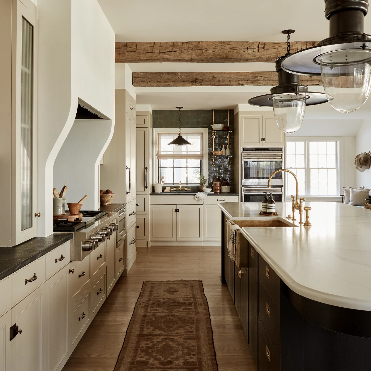 rustic kitchen with wood beams and industrial sconces and white cabinets and dark island