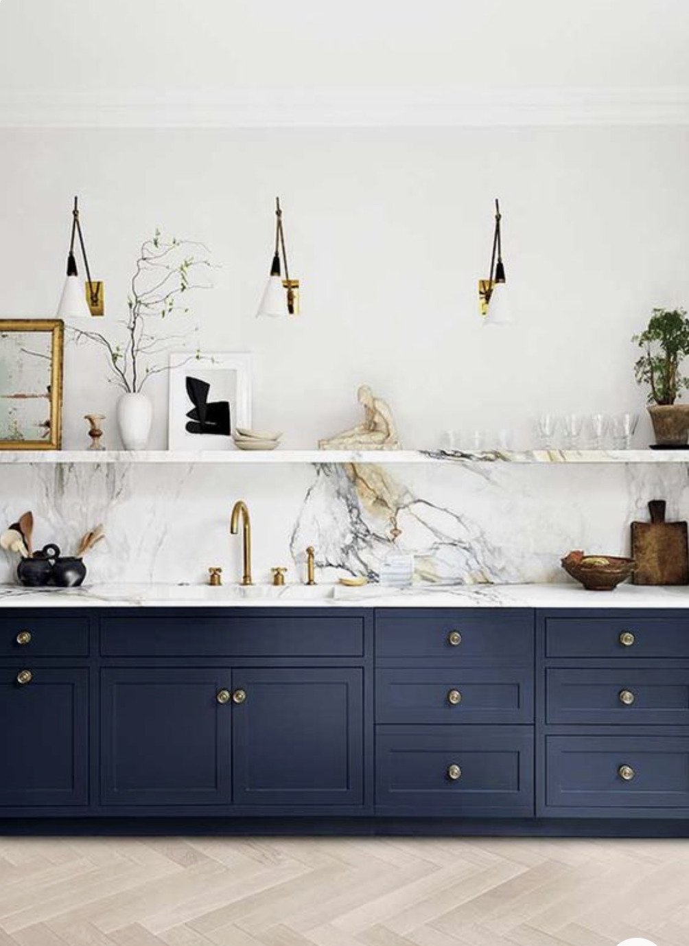 dark blue lower cabinets in kitchen with marble counter and backsplash ledge and wood herringbone floor