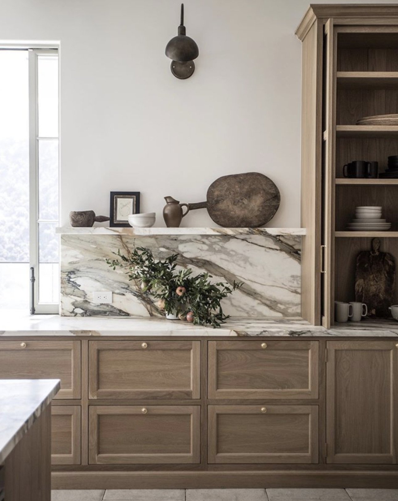 medium wood kitchen cabinets and marble counter with ledge holding rustic cutting board