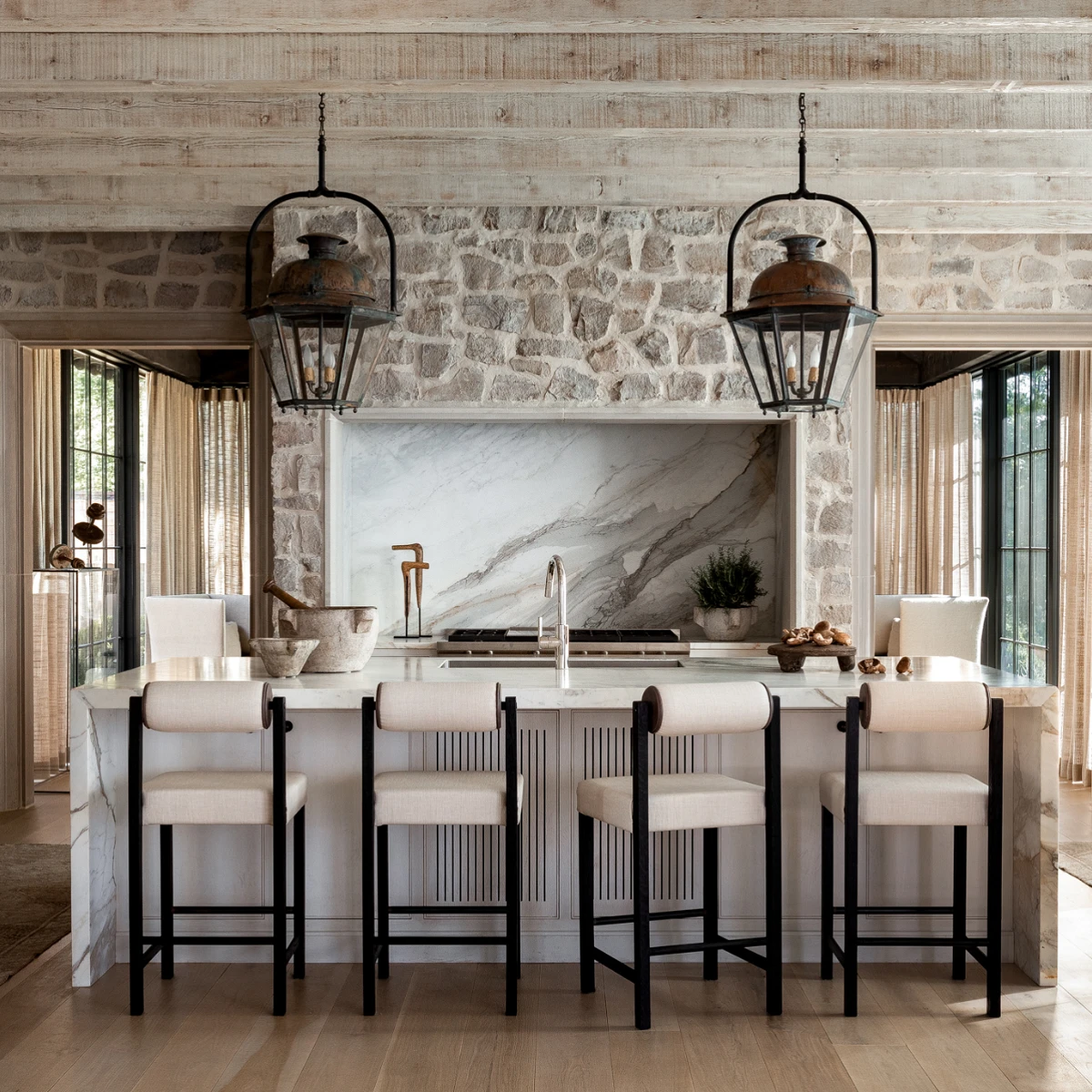 kitchen with rock wall surrounding stove and wood beams and large lanterns as pendants over island