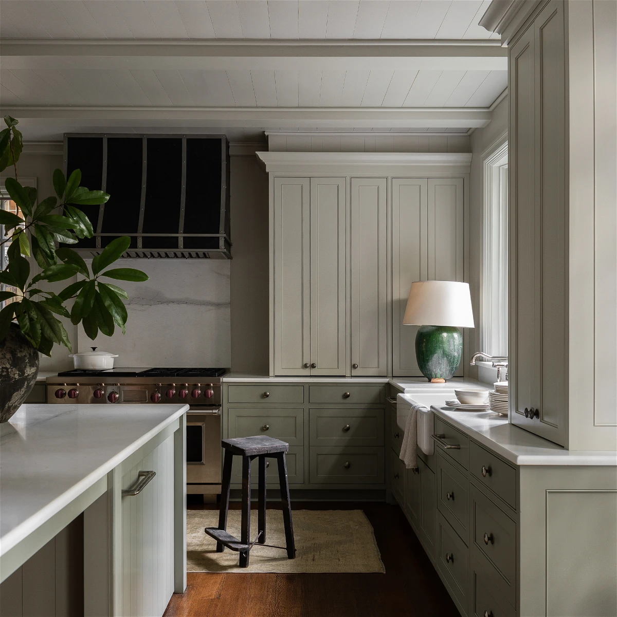 sage green kitchen cabinets with black hood and range and green table lamp on counter