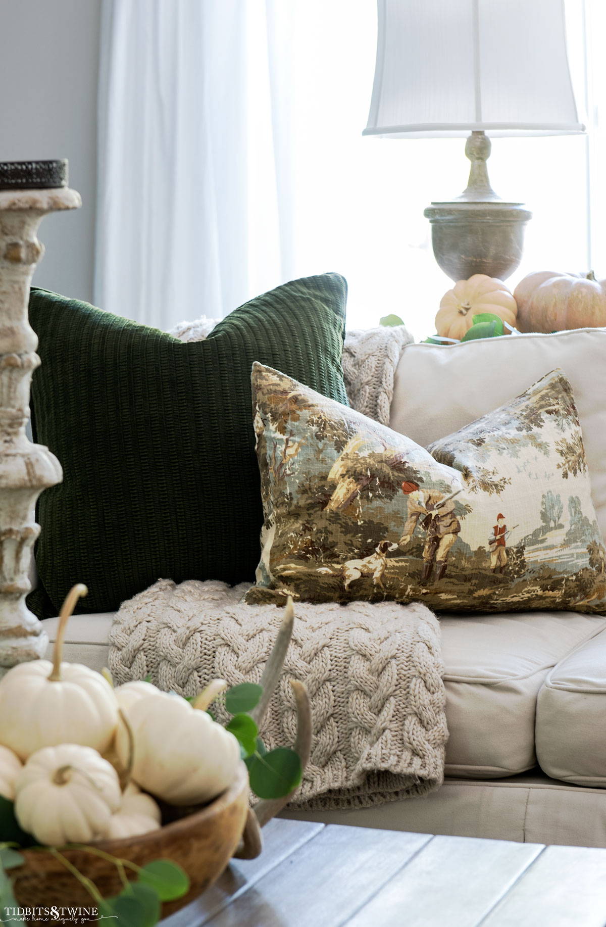 sofa styled with green fall pillows and knit throw and coffee table in front holding bowl of white pumpkins