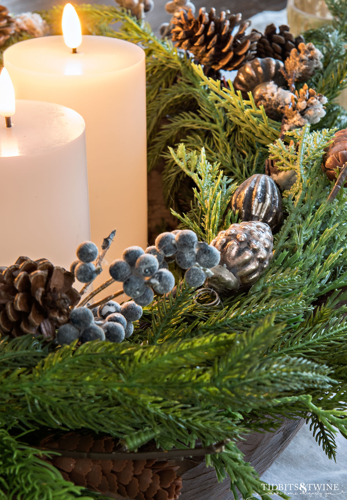 closeup of advent wreath with faux purple berries and faux greenery and mini ornaments with white candles