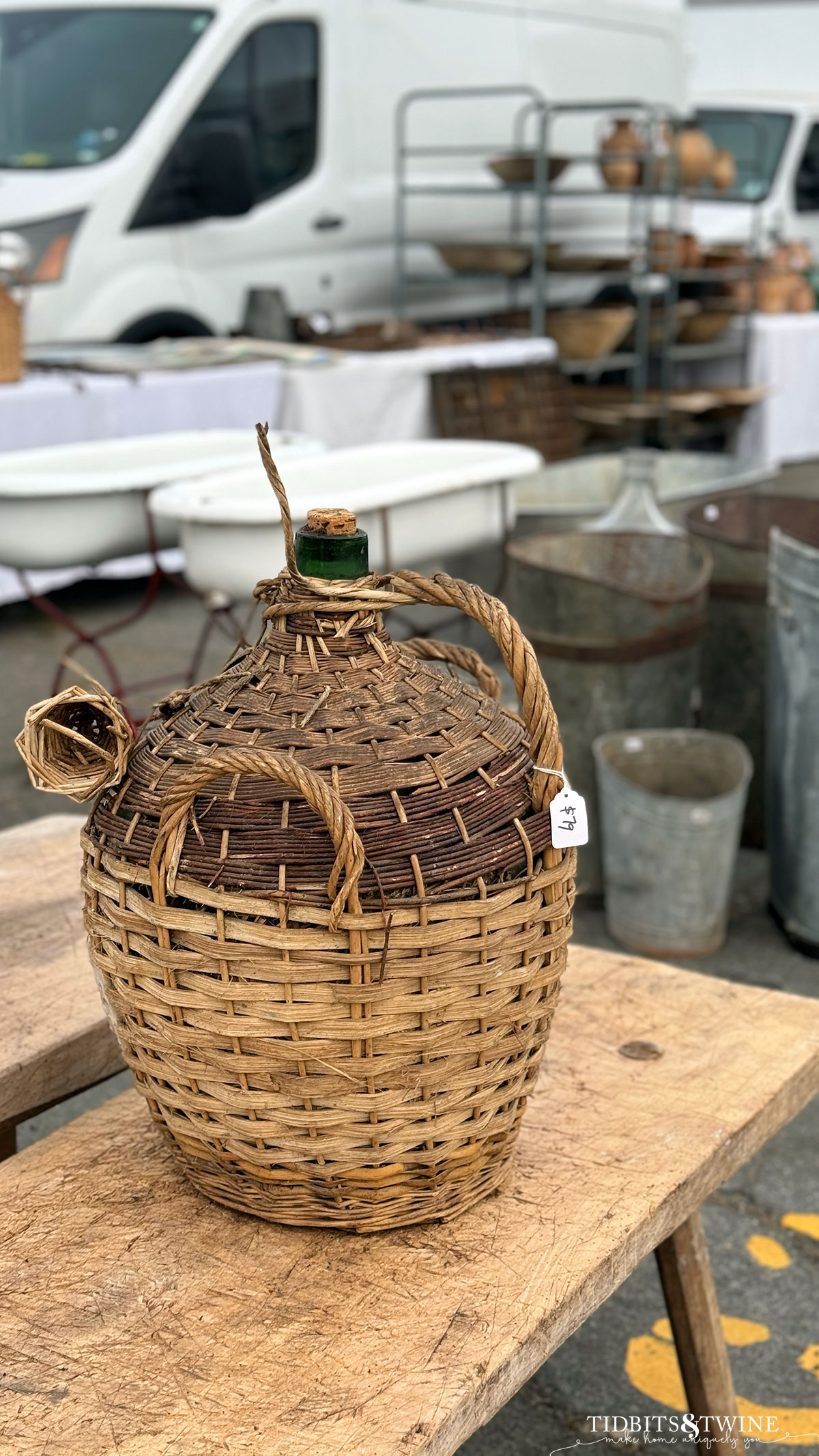 wicker demijon surrounding a green glass bottle on a wooden bench at an antique fair