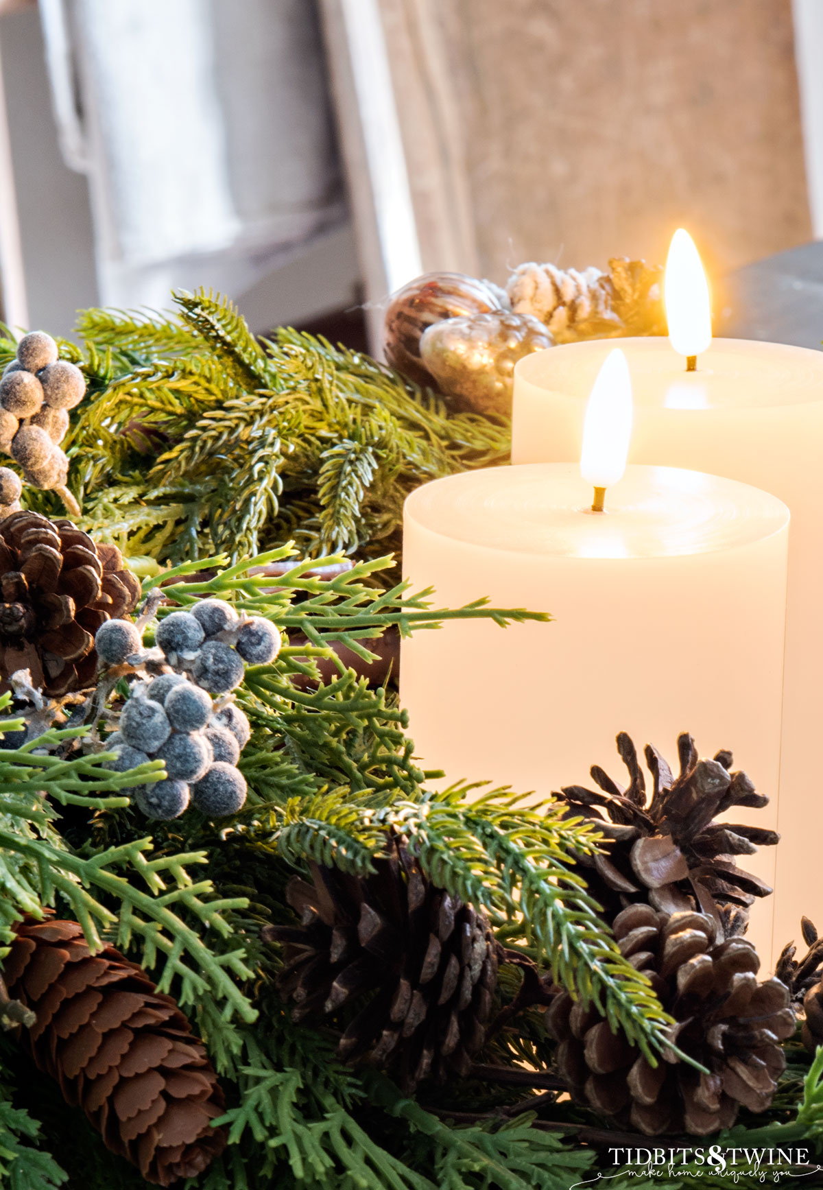 closeup of advent wreath with greenery pinecones berries and ornaments and white pillar candles