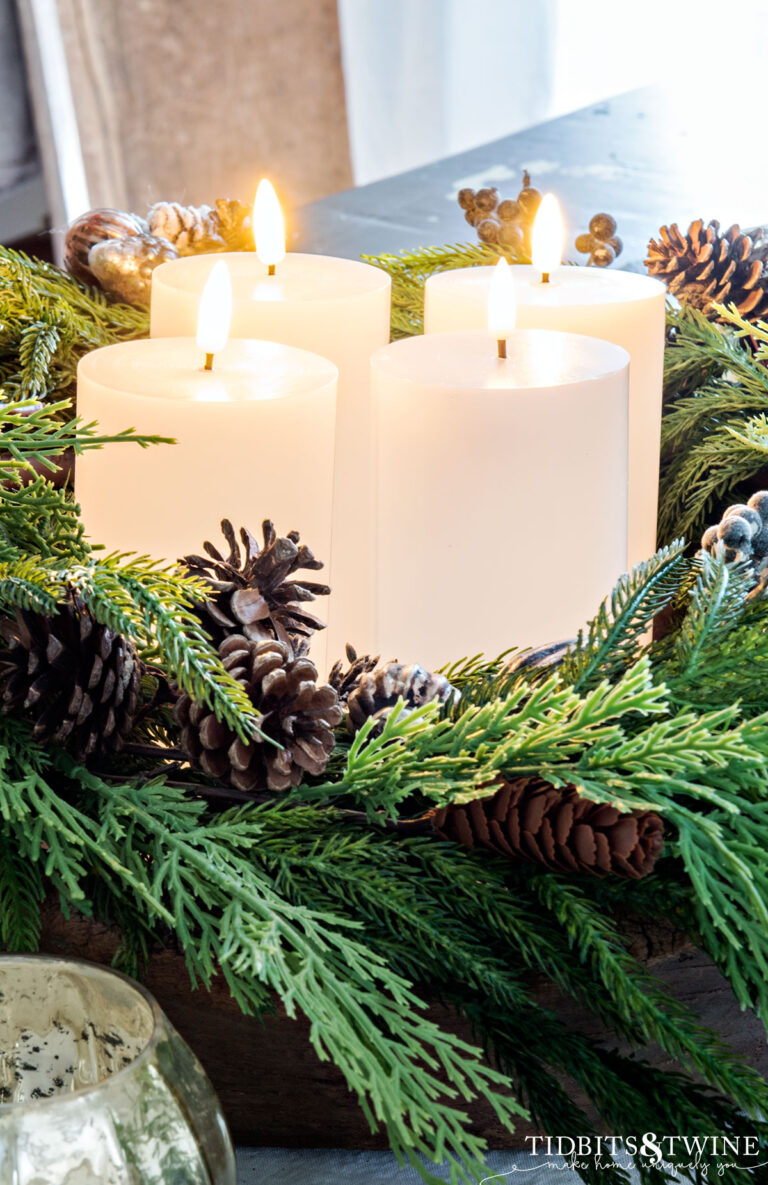 four white led pillar candles inside a wreath of greenery with pinecones on dining table