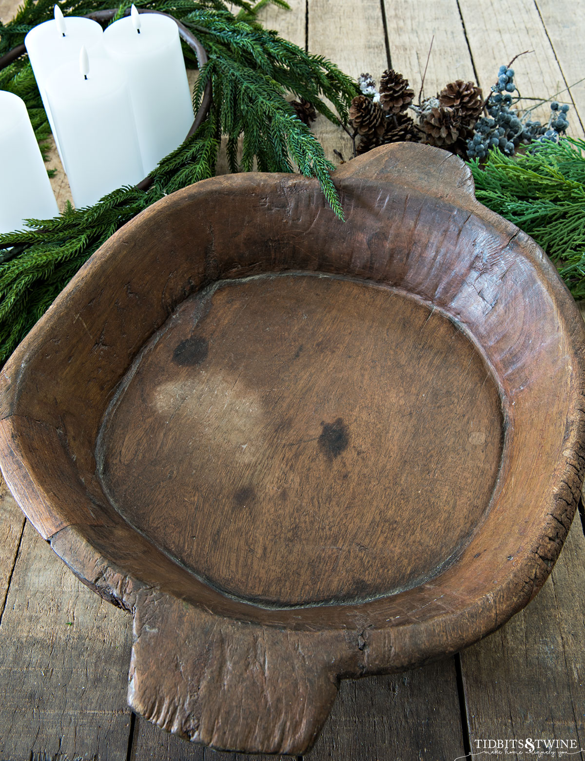 brown rustic shallow round dough bowl on table with norfolk pine garland and candles in background