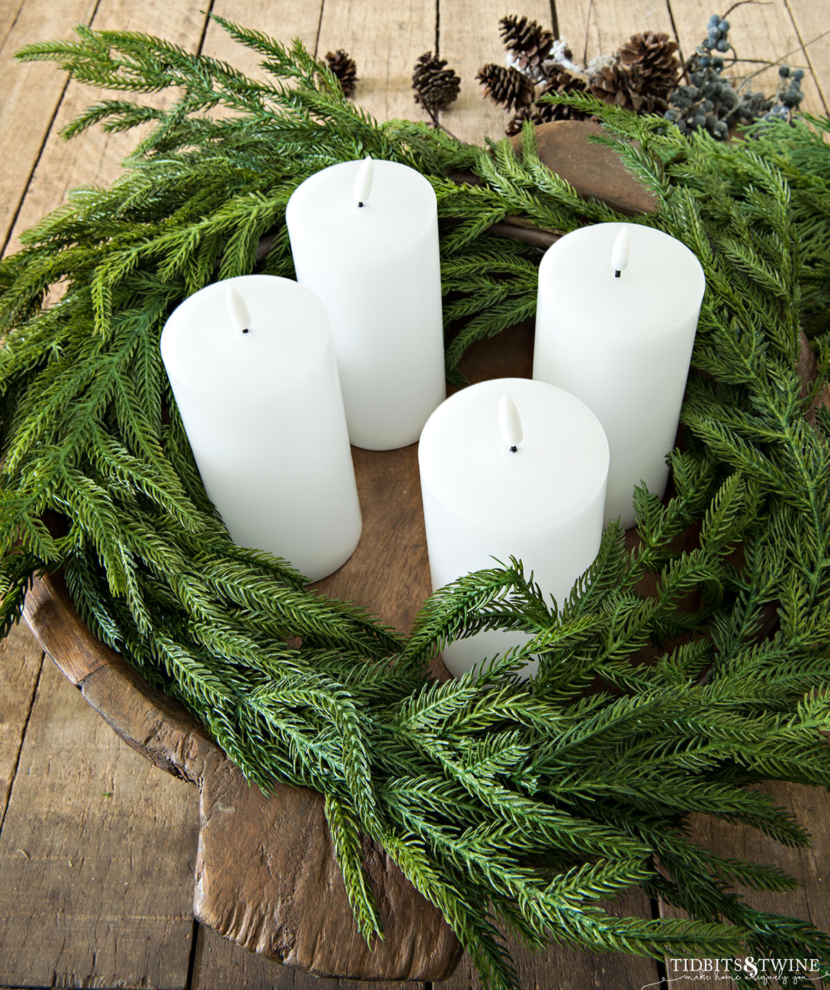 round dough bowl with norfolk pine garland wrapped inside and four white pillar led candles in the middle