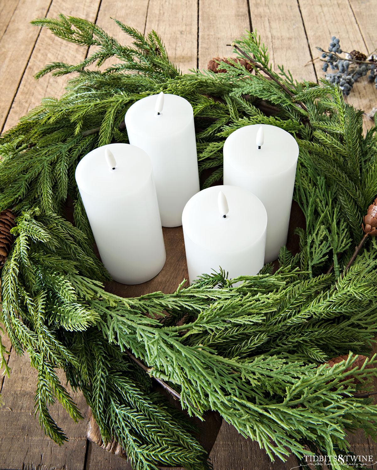 round dough bowl with norfolk pine and cedar branches wrapped inside and four white pillar led candles in the middle