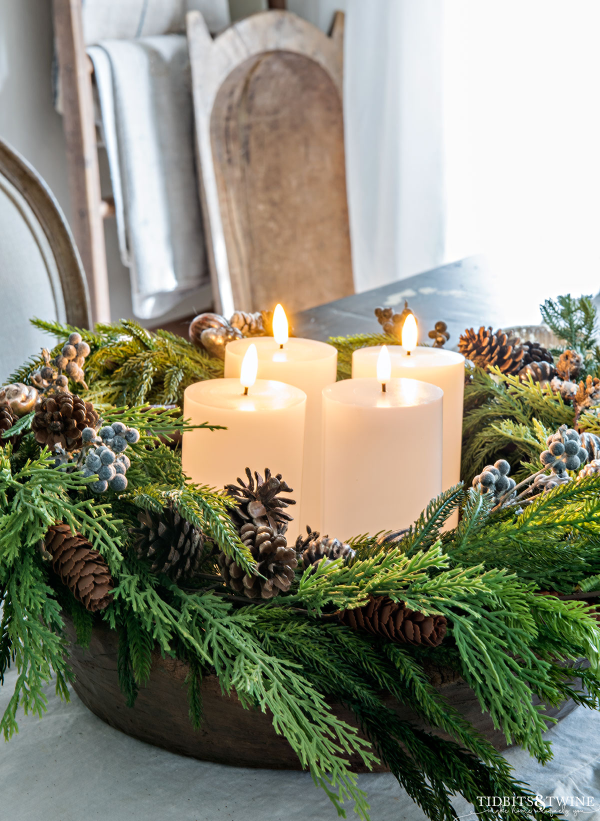 shallow dough bowl with greenery and pinecones and white pillar candles in center