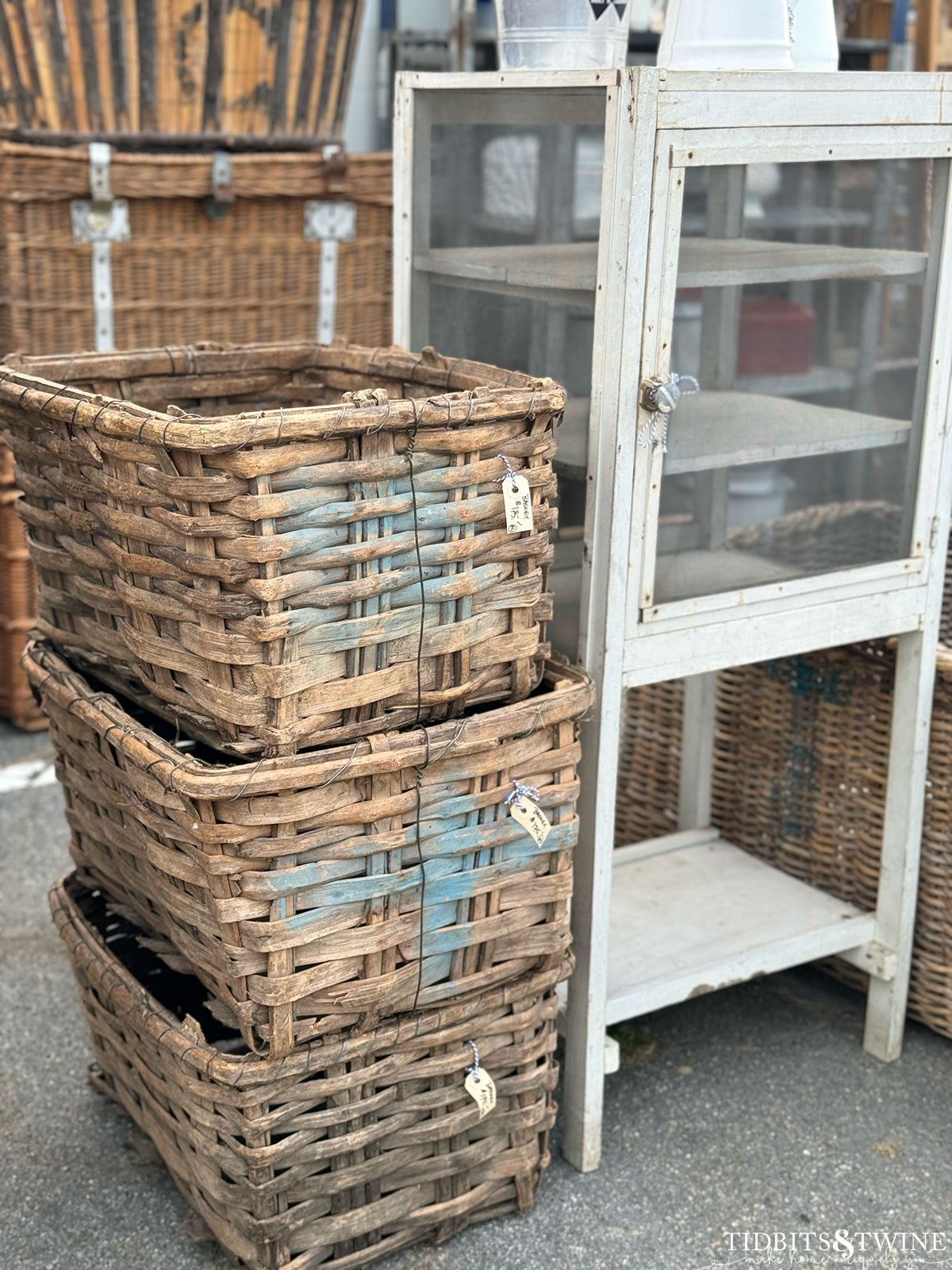 stack of antique french baskets with blue paint on the ends next to an antique medicine cabinet at an antique fair