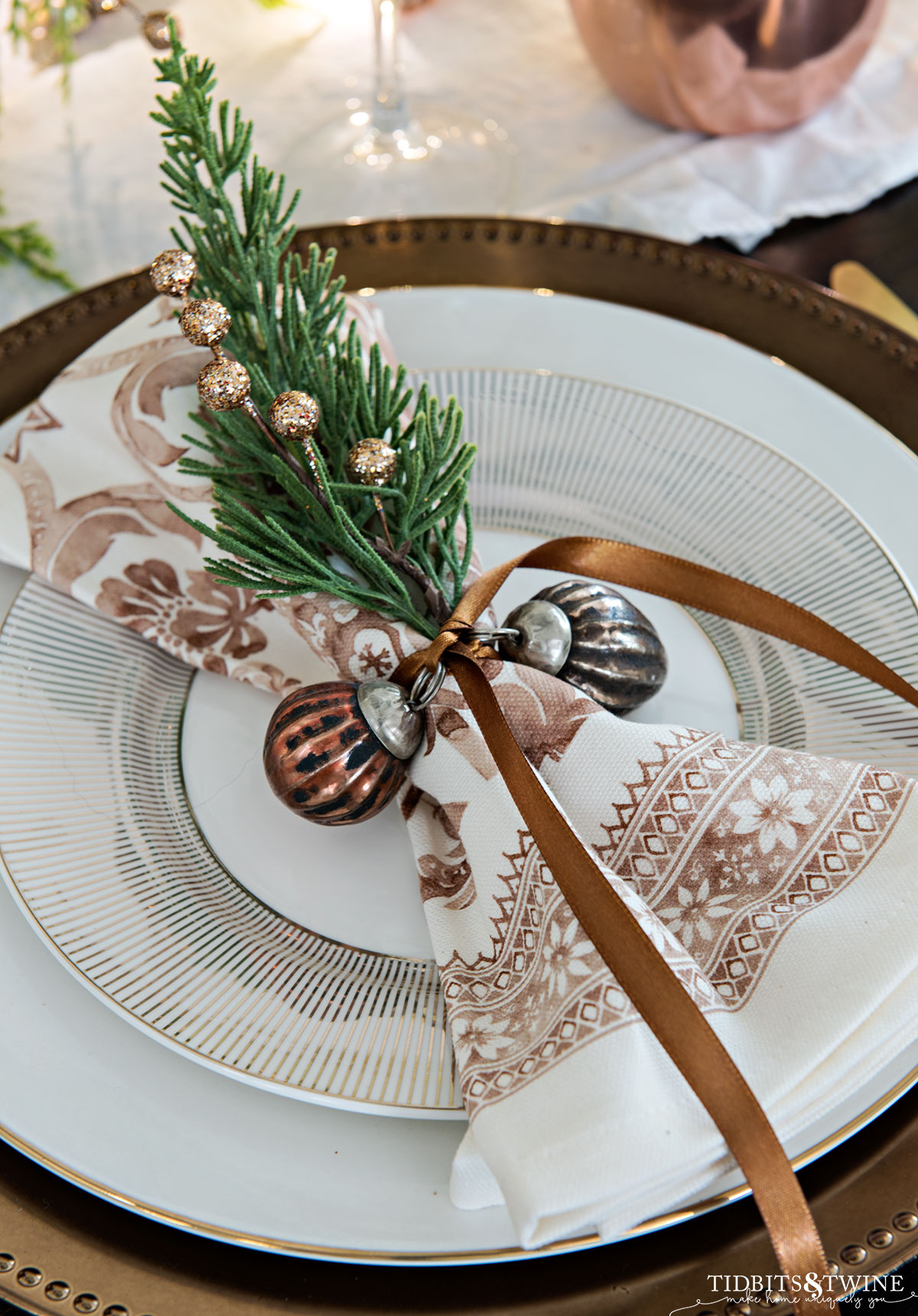copper christmas tablescape with gold stripe plates and bronze napkins tied with greenery