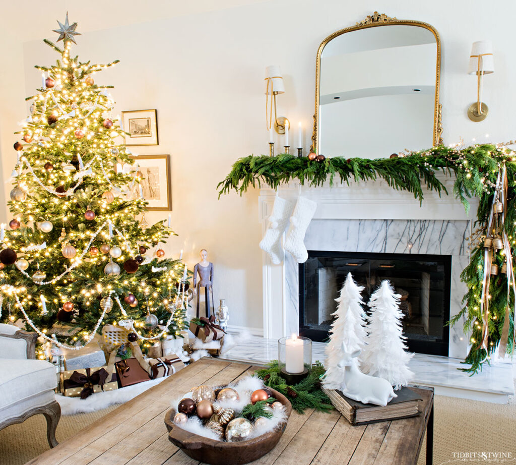 neutral christmas living room with gold mirror above fireplace and christmas tree in corner