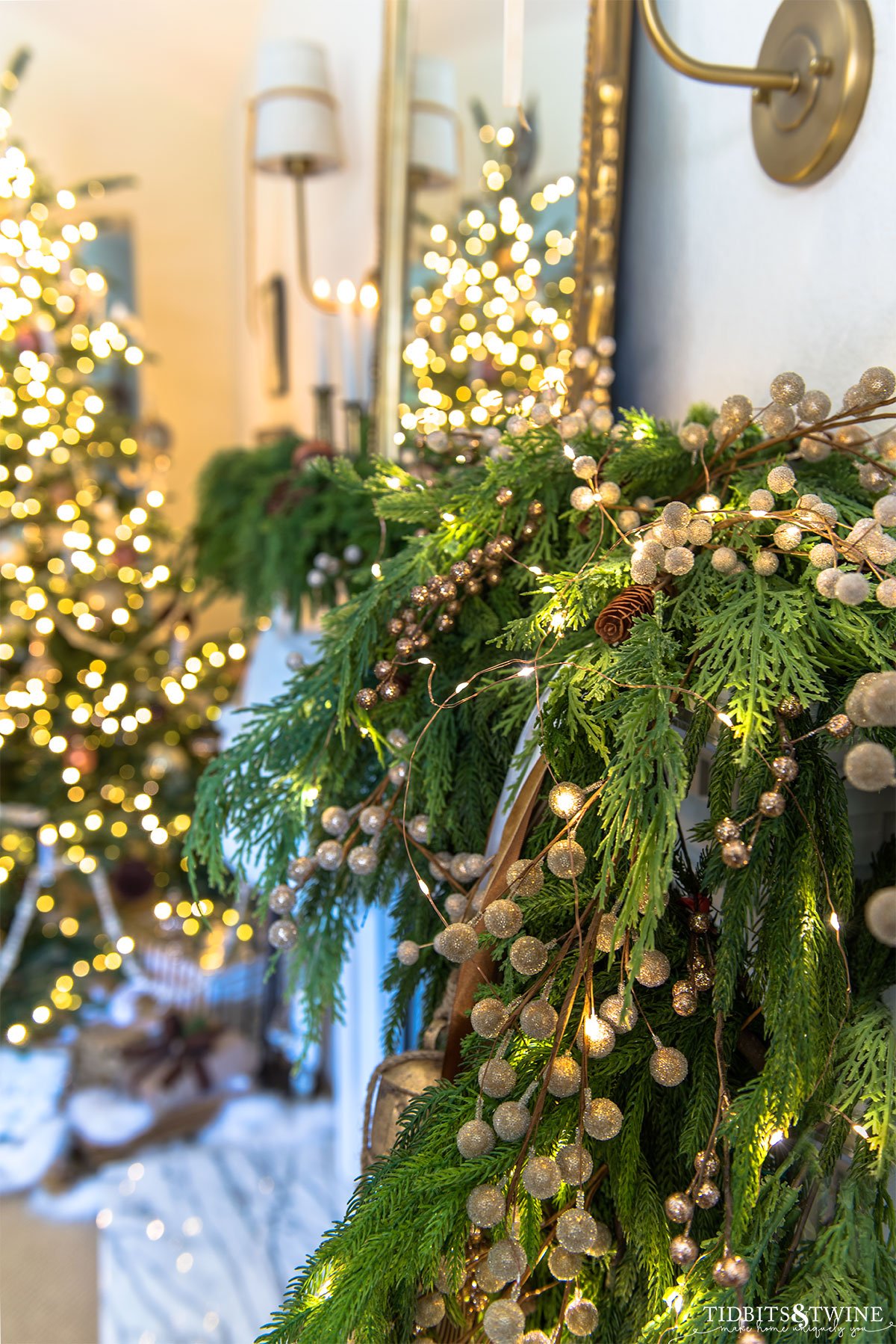 closeup of french fireplace garland with glitter picks, bells, ribbon and lights with christmas tree in background