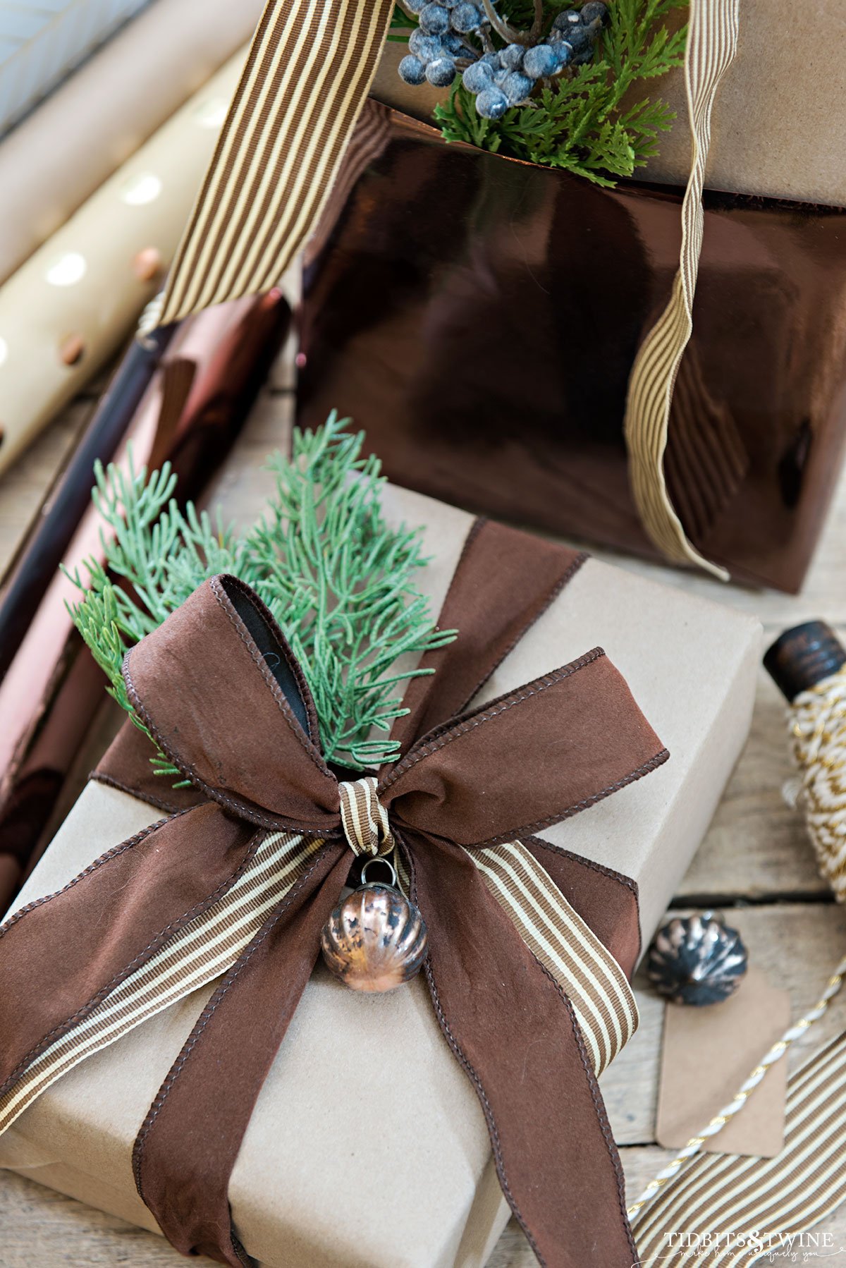 closeup of christmas present wrapped in brown paper with brown striped ribbon and small ornament on the bow