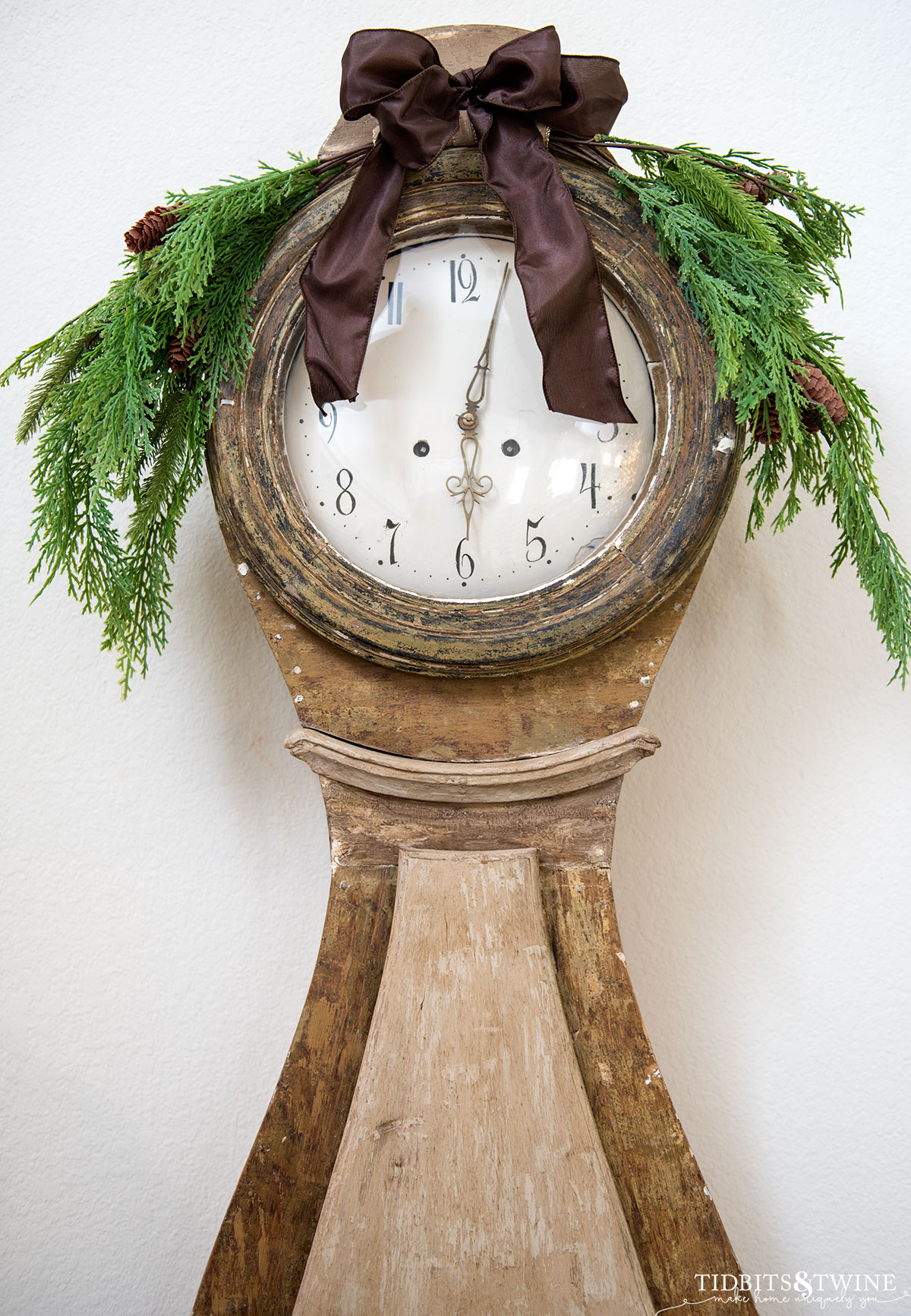 beige antique mora clock with faux cedar swag on top with brown ribbon bow for Christmas