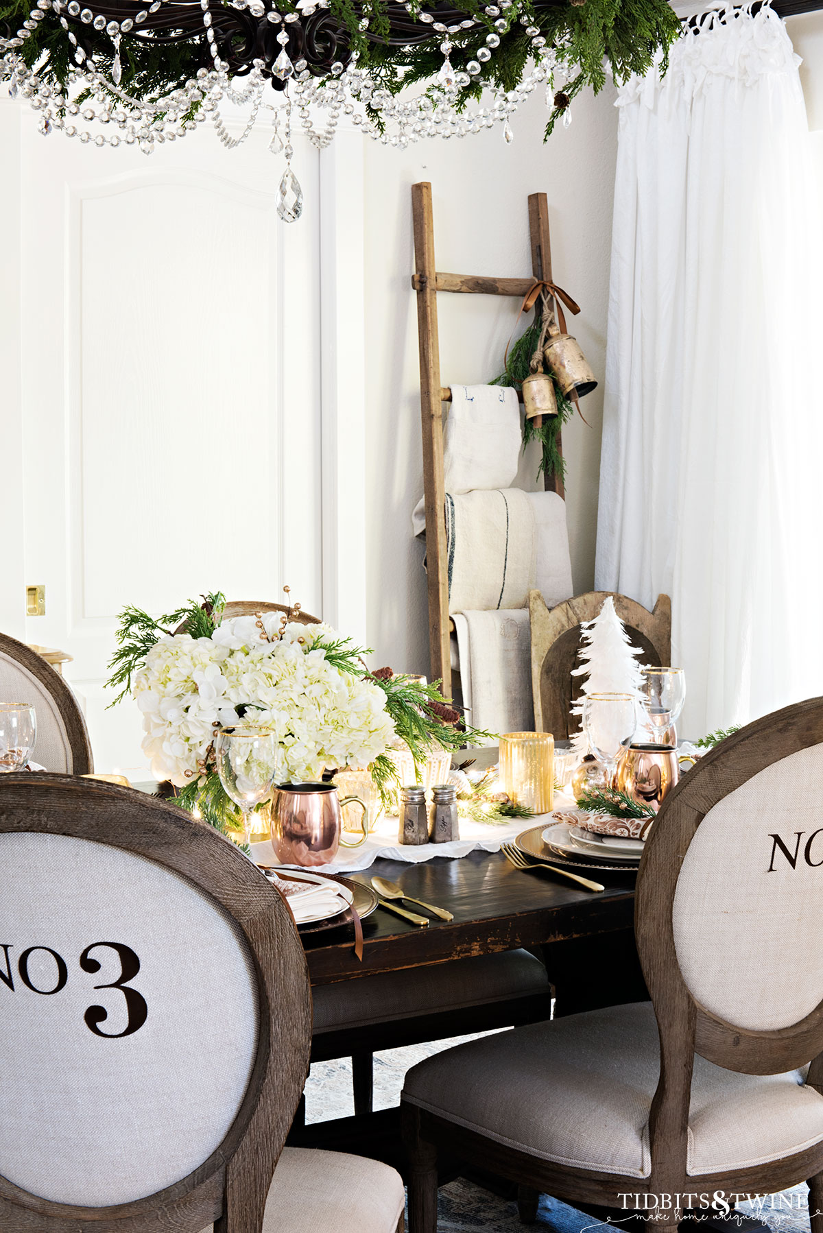 french christmas dining table with garland on chandelier, numbered dining chairs and white hydrangea centerpiece