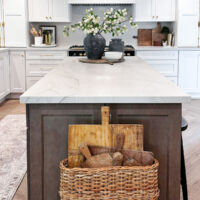 white kitchen with brown island an black range and basket of breadboards by island
