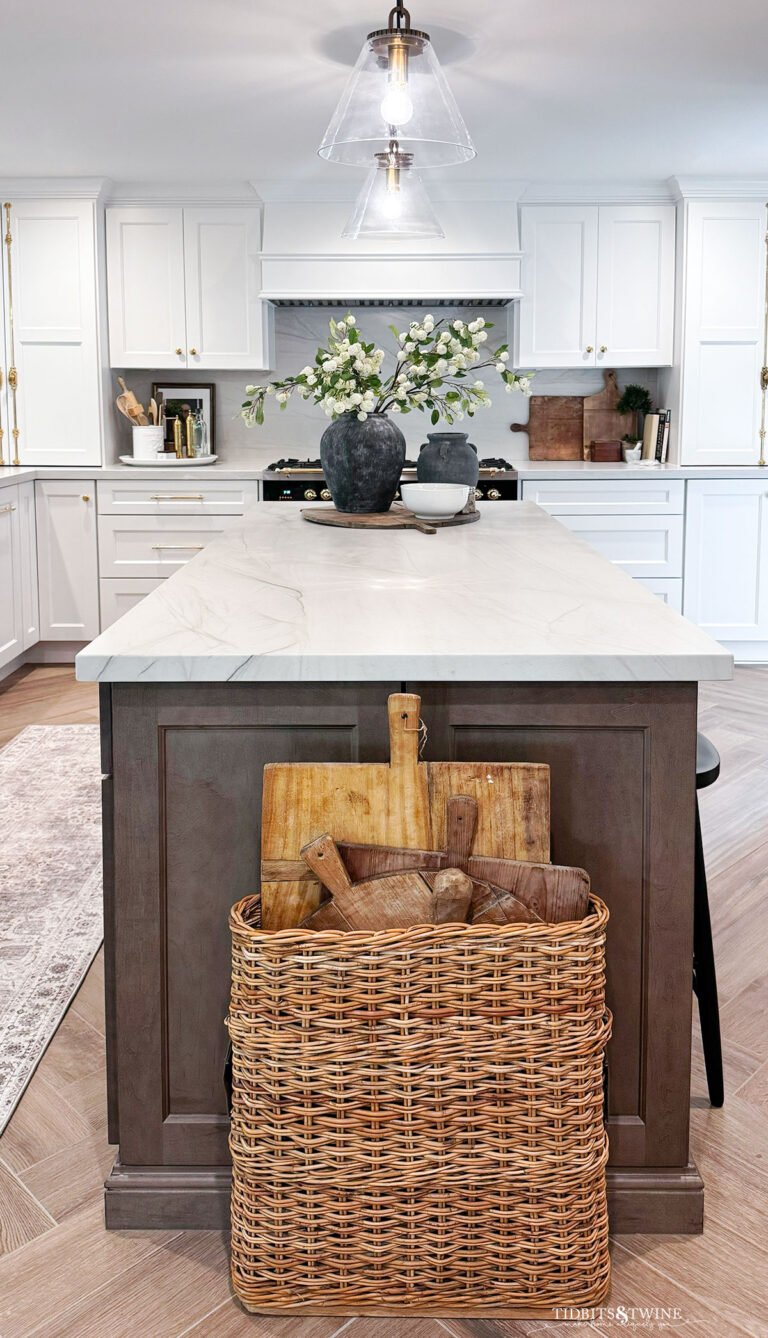 white kitchen with brown island an black range and basket of breadboards by island