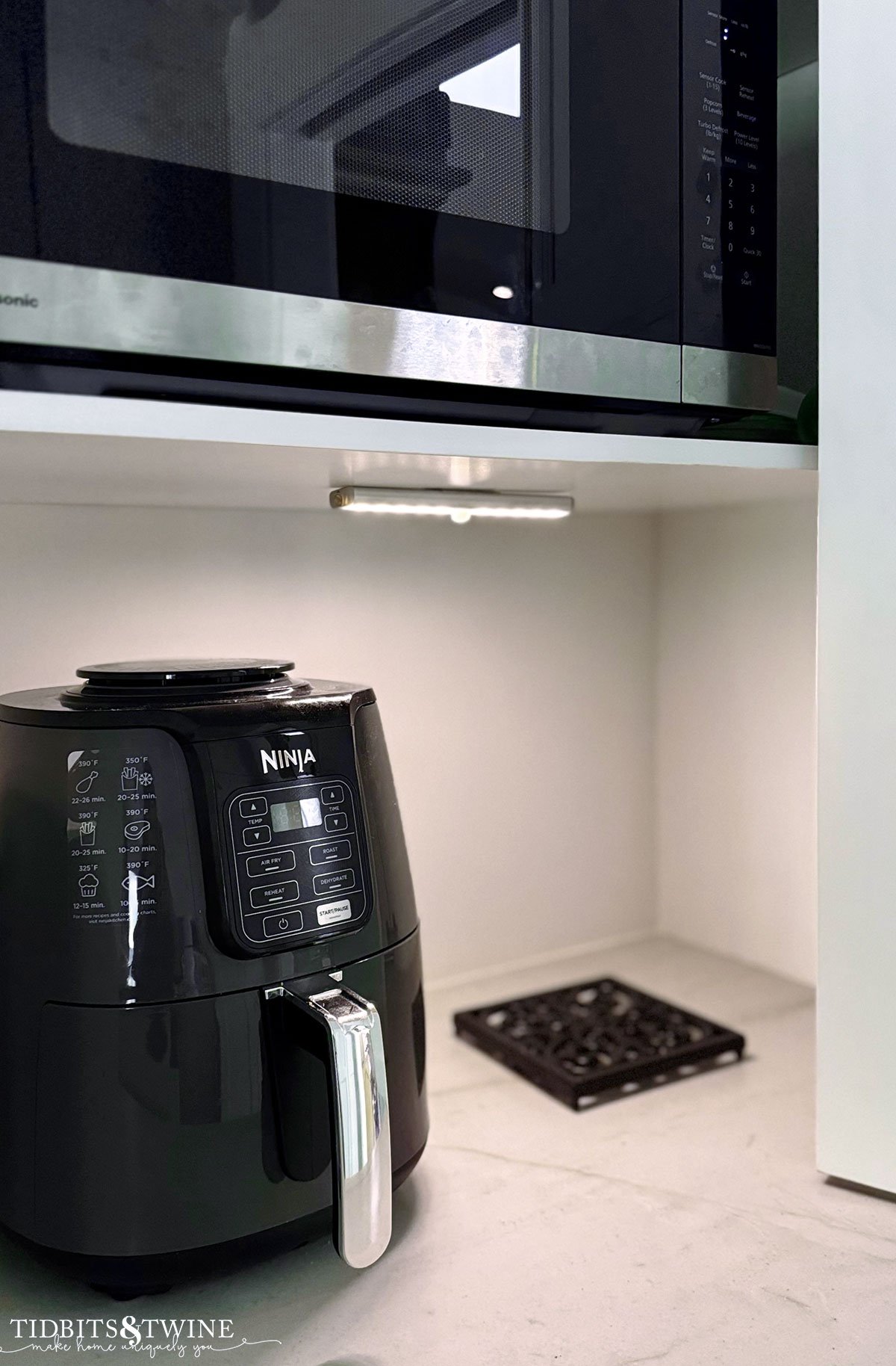 black ninja air fryer in kitchen cabinet with light and microwave above