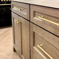 brown wood kitchen island with brass knobs and pulls and herringbone floor black ILVE stove