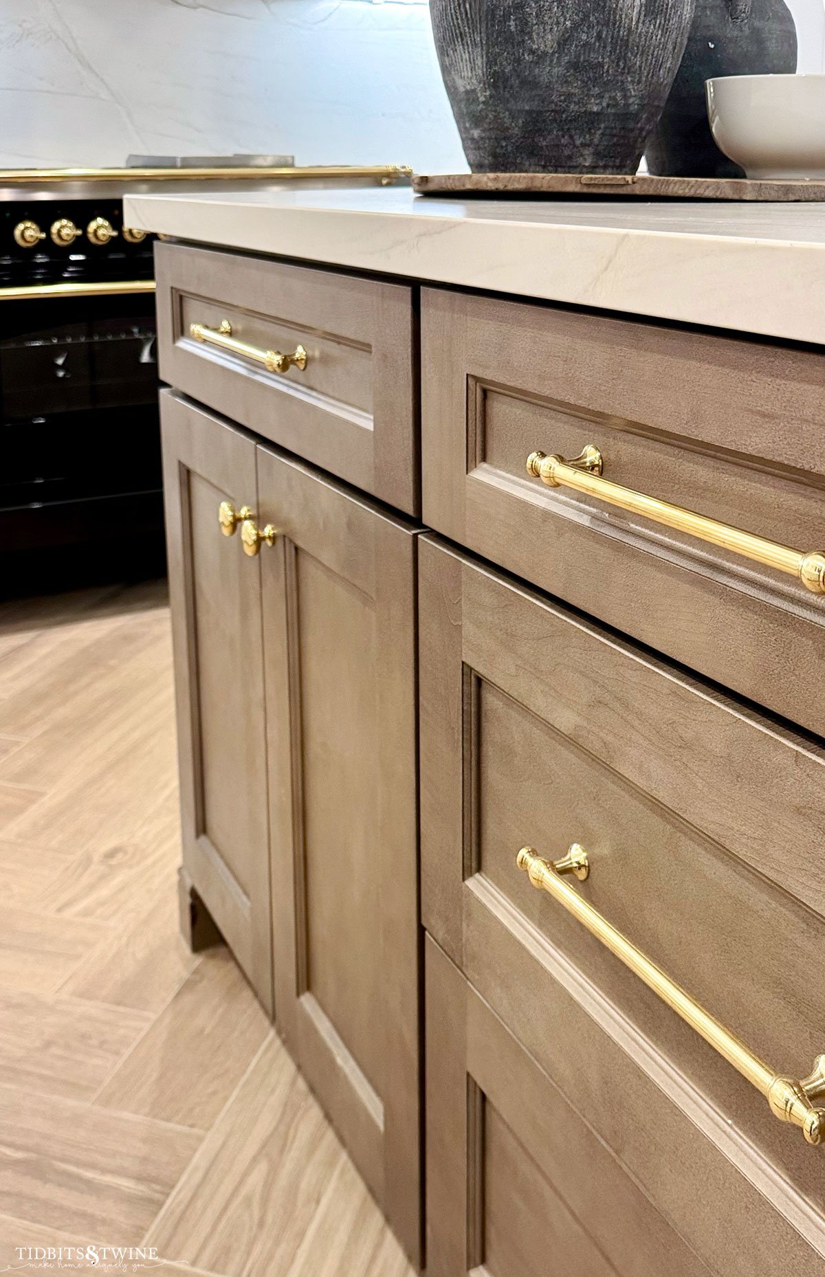 brown wood kitchen island with brass knobs and pulls and herringbone floor black ILVE stove