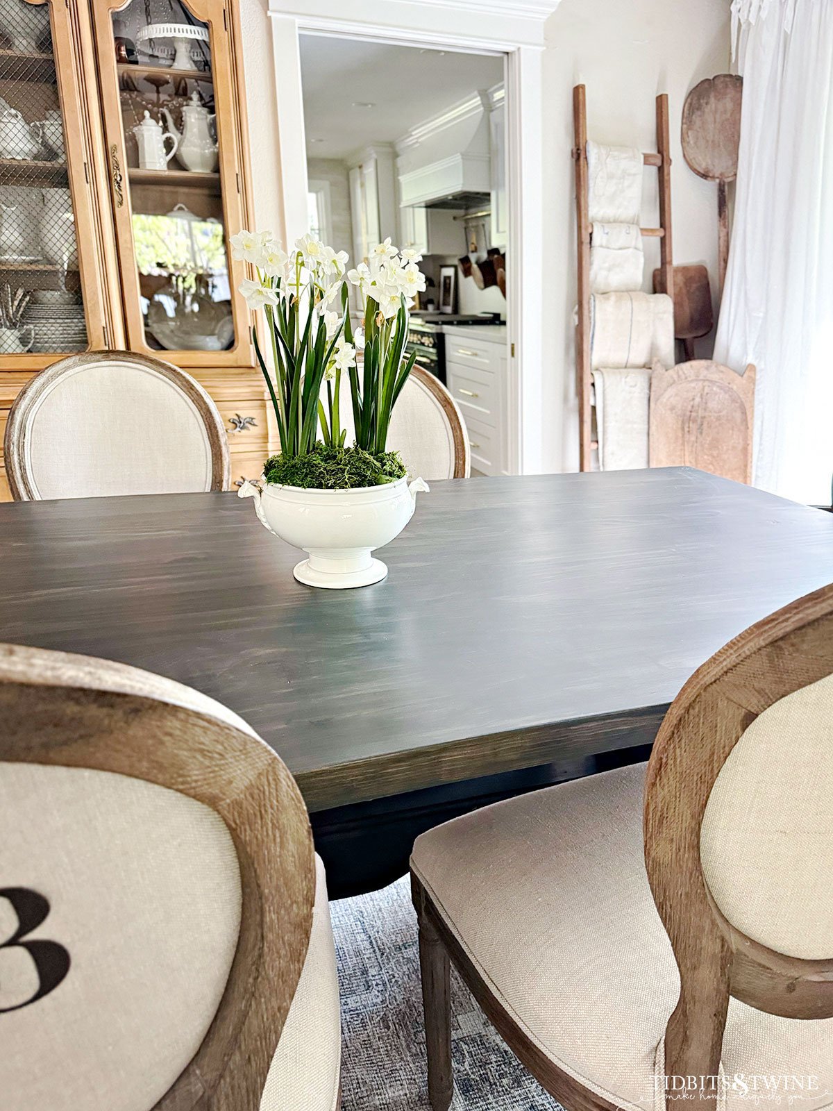 neutral french country dining room with paperwhites on dining table and hutch of ironstone