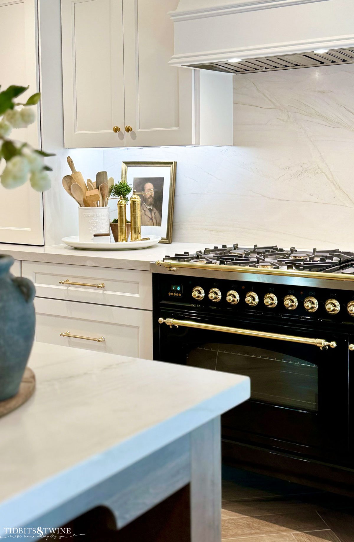 white cabinets with quartzite counter and backsplash and glossy black ILVE range with brass hardware