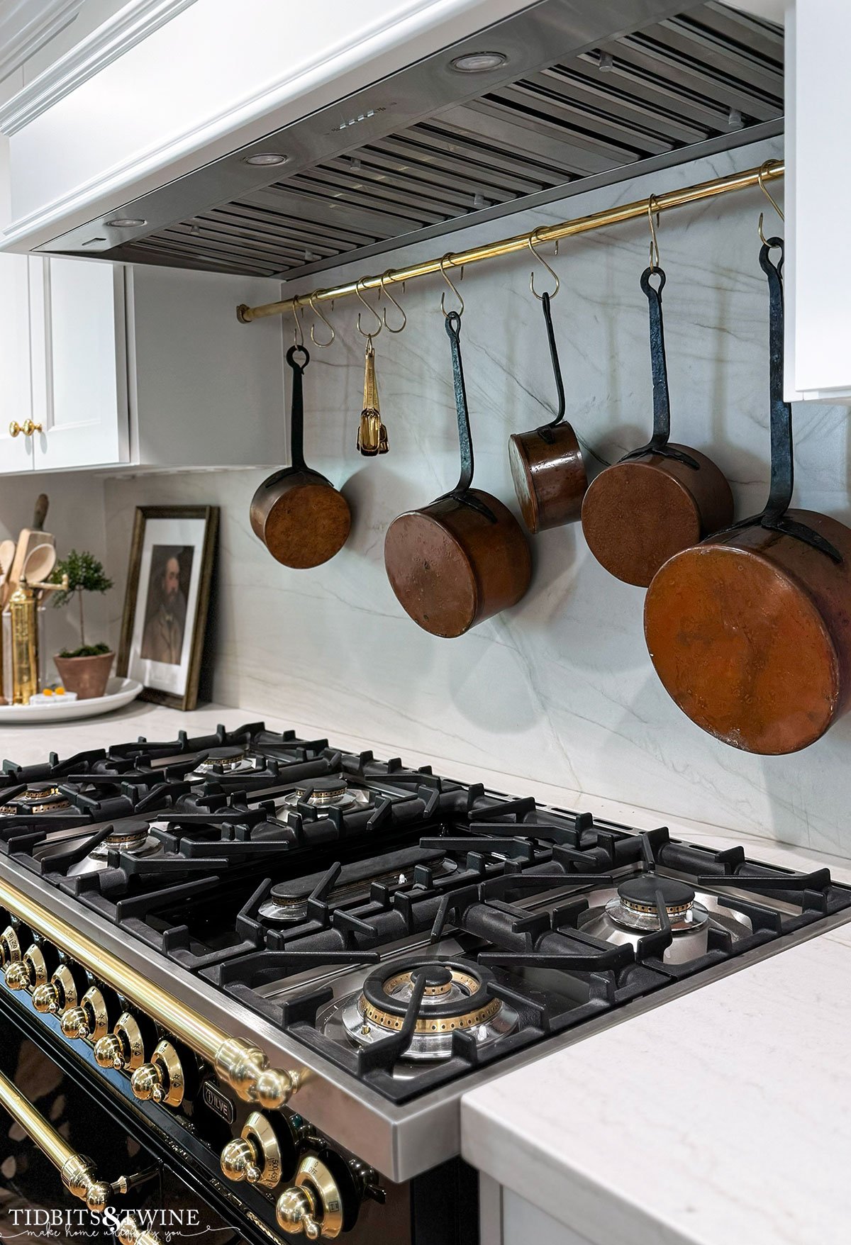 brass pot rail hanging above black range with antique copper pots hanging from it