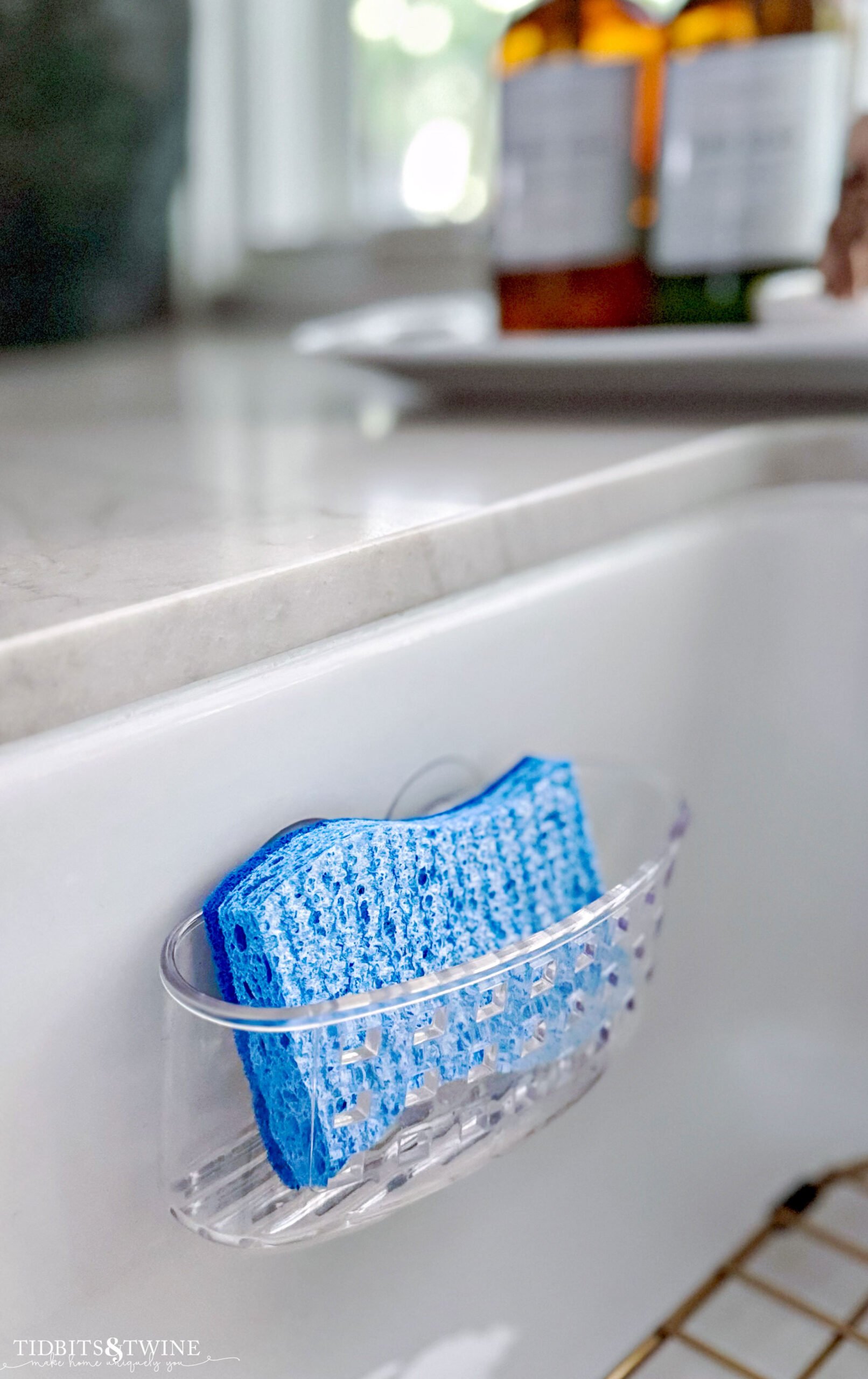 clear plastic sponge holder on side of white kitchen sink holding blue sponge