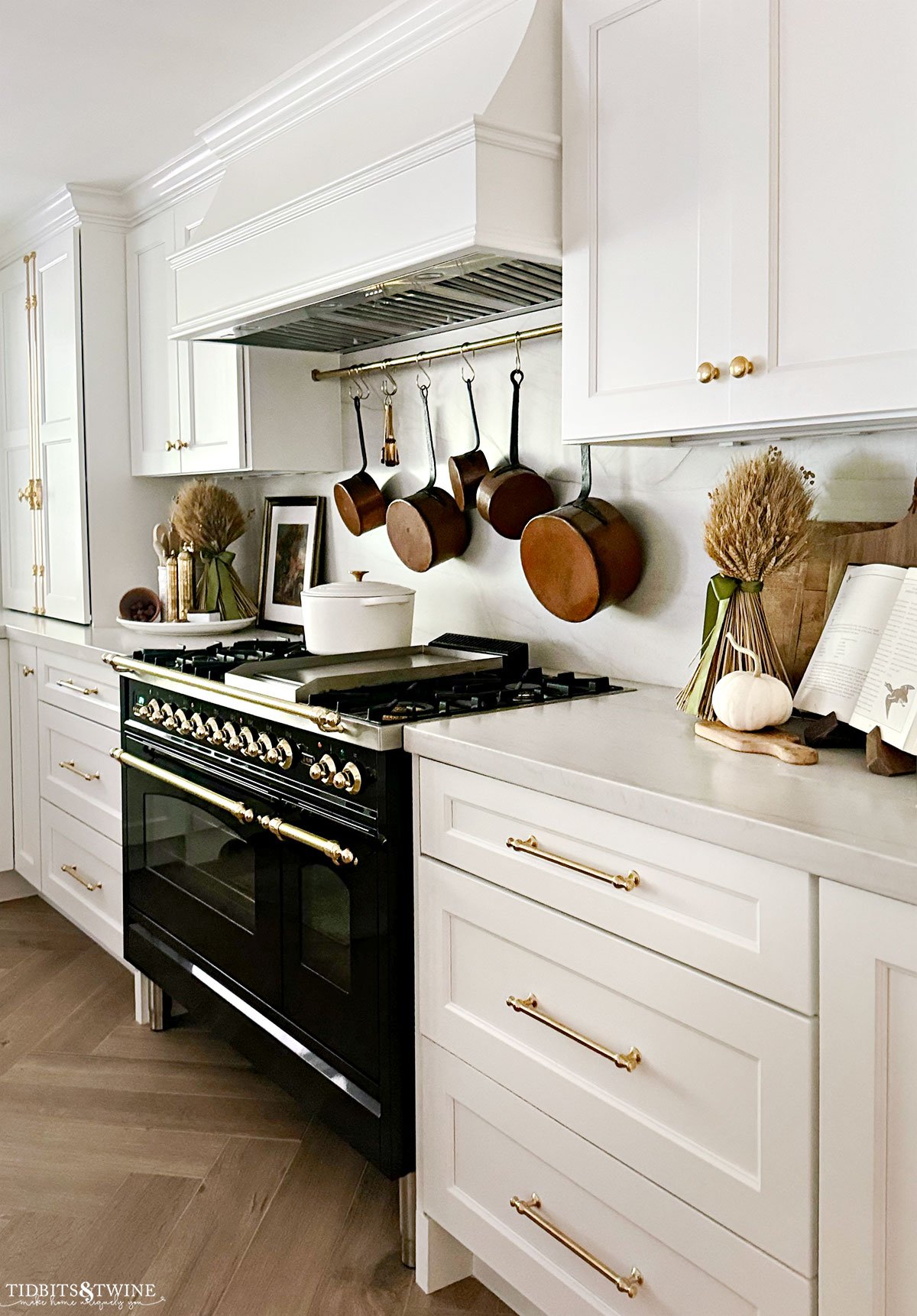 white kitchen with herringbone wood floors and glossy black ilve range decorated for fall