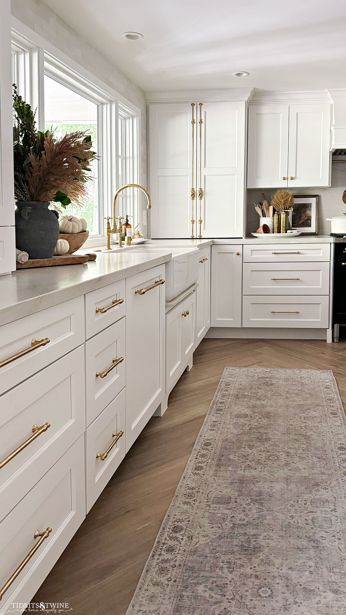 white kitchen with large picture window decorated for fall with greenery and pampas grass and washable runner on herringbone floor