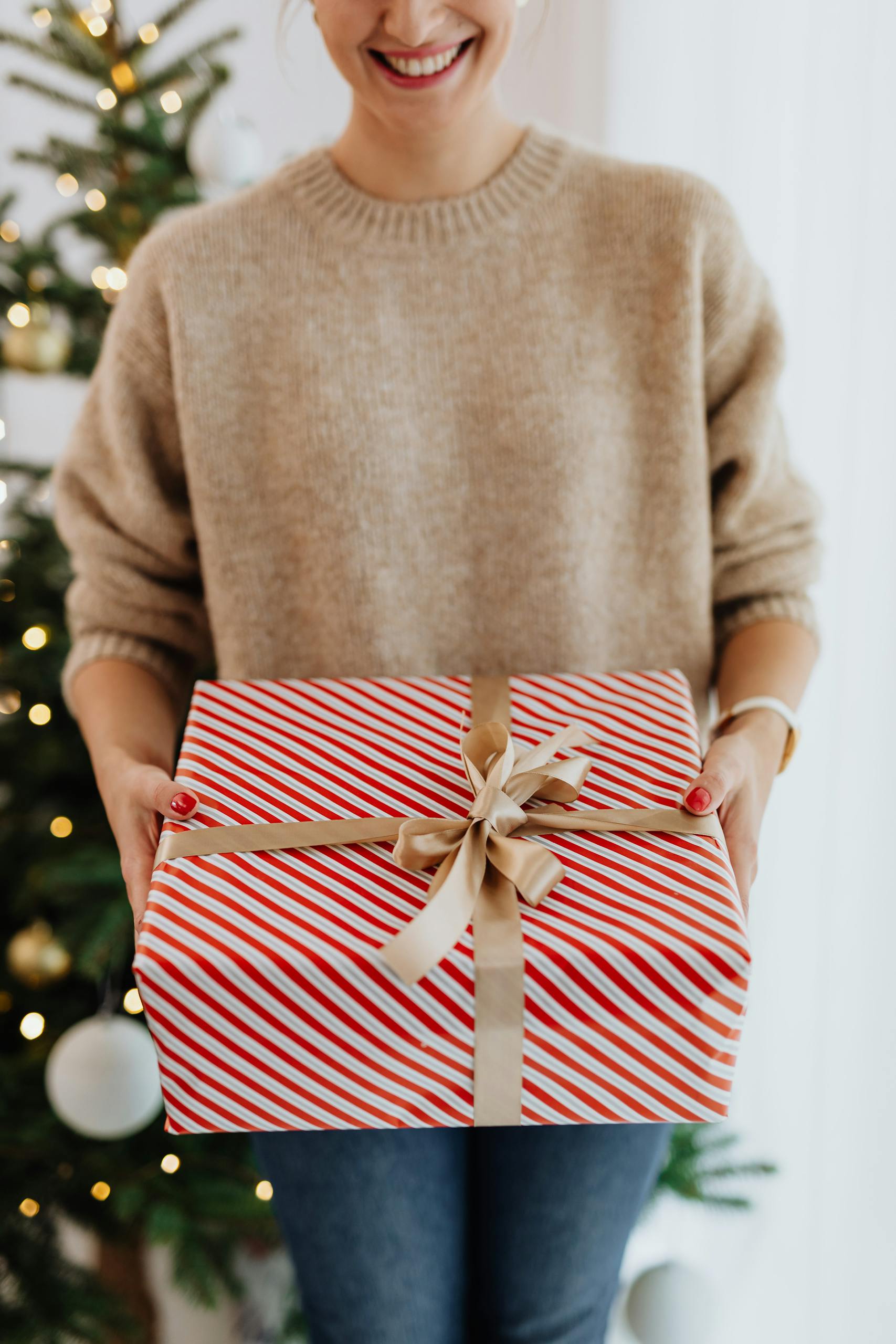 Close-up of a woman holding a beautifully wrapped Christmas gift with a tree in the background.