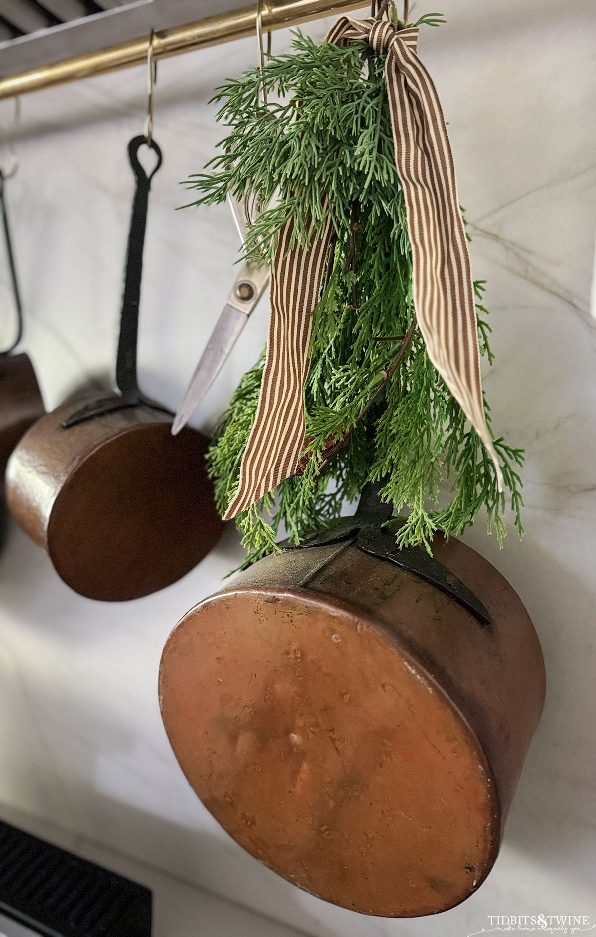 antique copper pot hanging on pot rail with greenery for Christmas