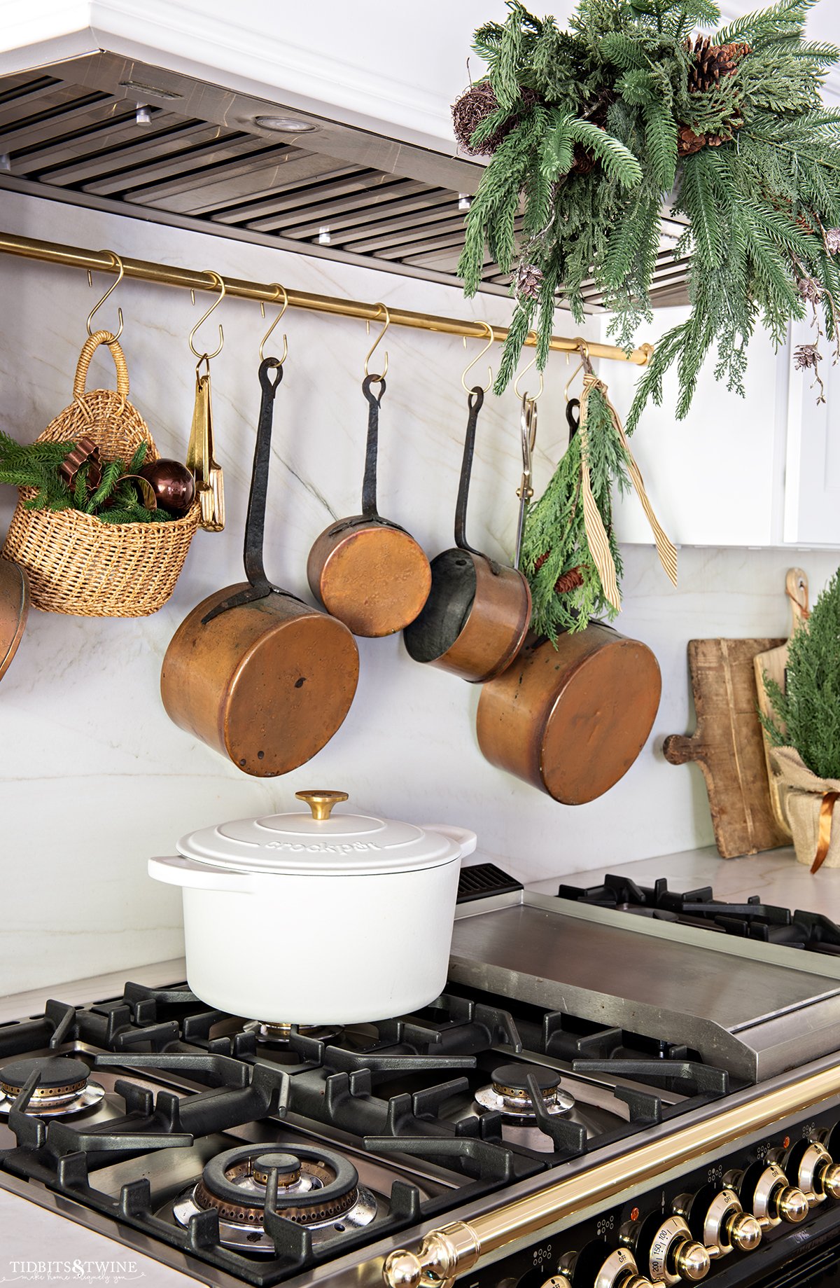 brass pot rail with copper pots above black stove with greenery for Christmas kitchen