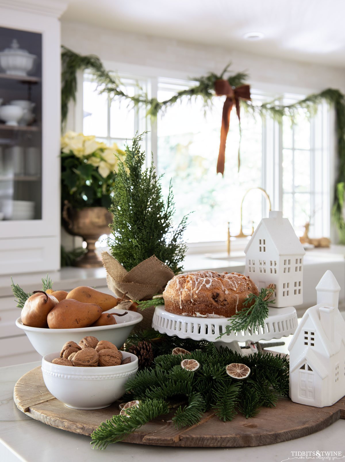 Christmas display on kitchen counter with greenery fruit nuts and white houses - Decorating Ideas for Christmas